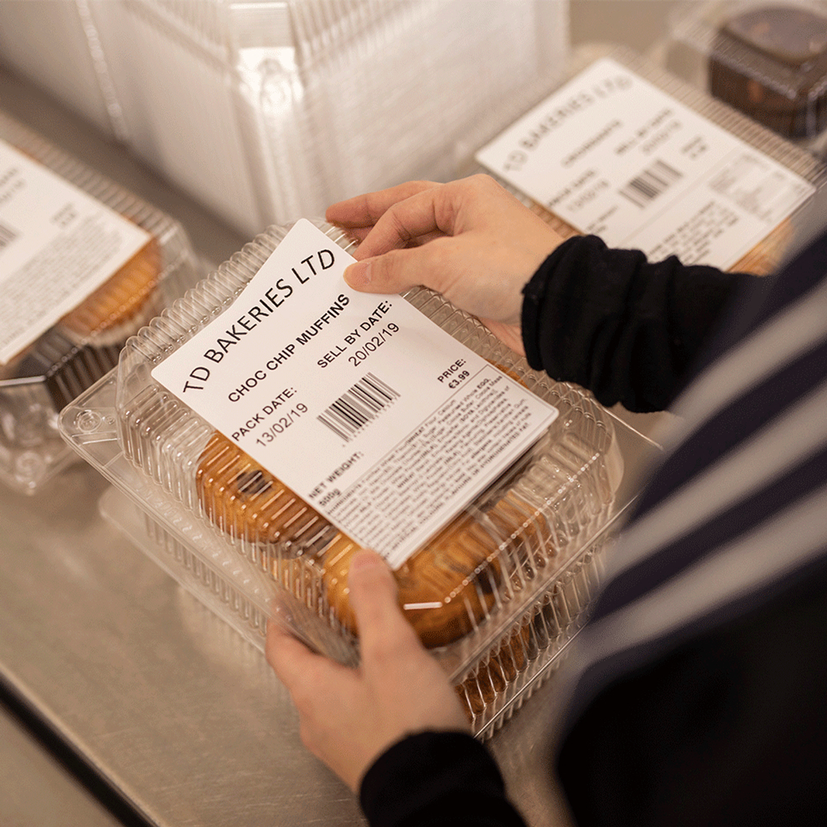 Eine Person hält einen Behälter mit Muffins und betrachtet das Etikett. Der Behälter ist im Fokus.