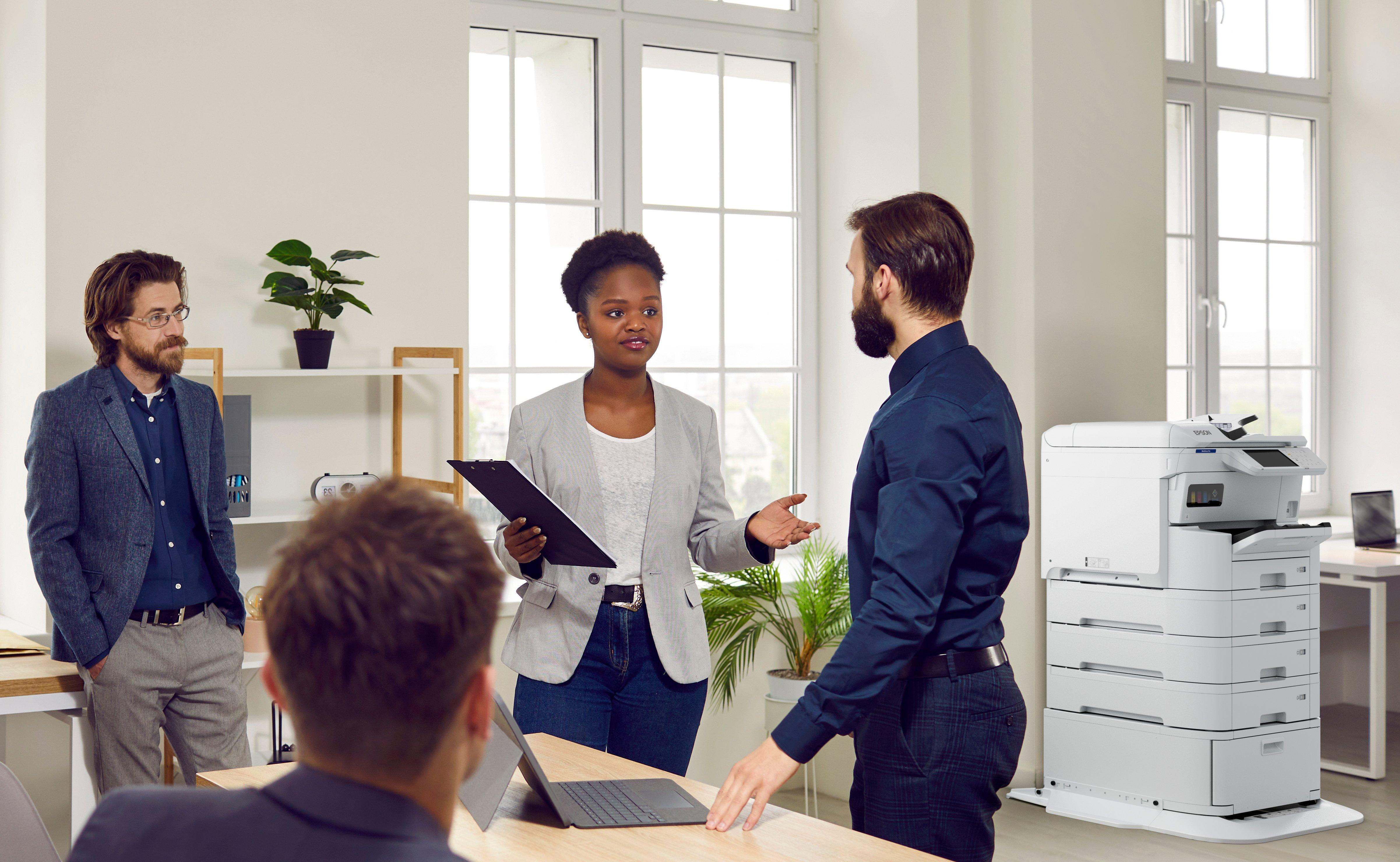 Trzy osoby zgromadziły się w pobliżu drukarki w biurze.