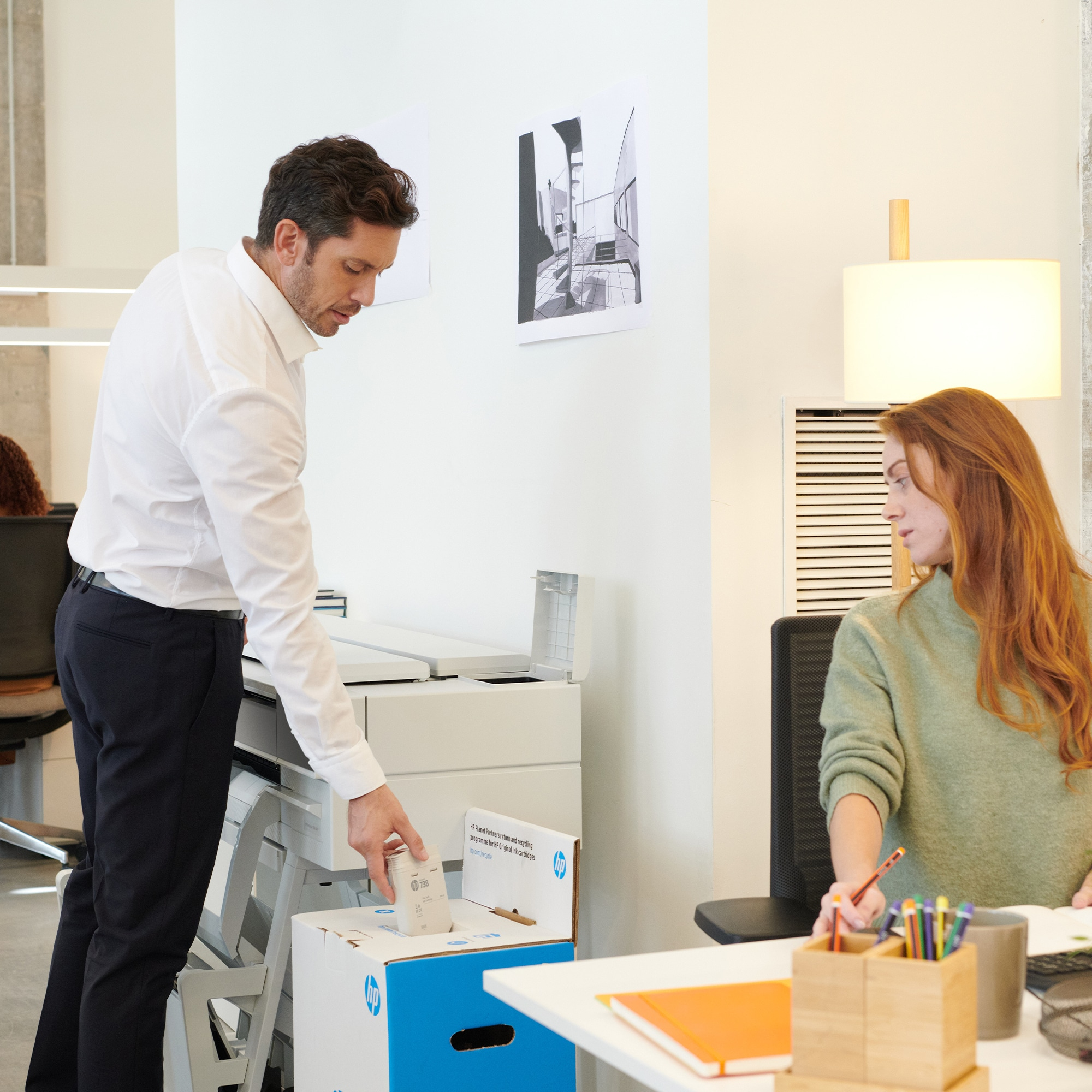 Un homme en chemise blanche utilise une imprimante dans un bureau avec une femme à proximité.