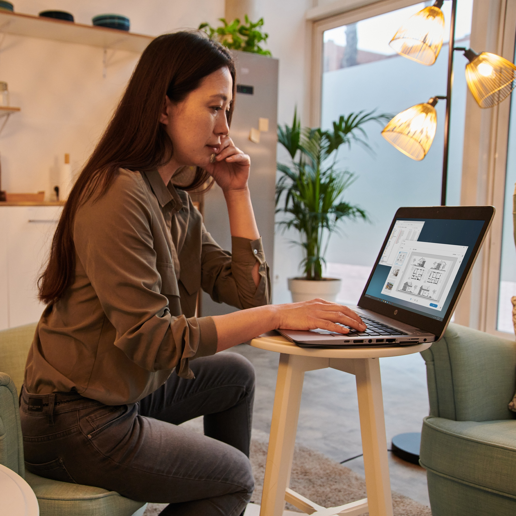 Une femme travaille sur un ordinateur portable à la maison avec des plantes et une lampe en arrière-plan.