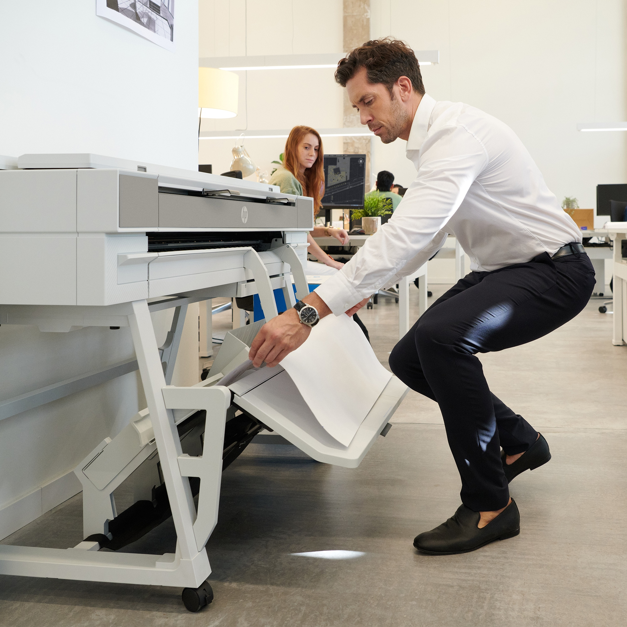 Un homme en chemise blanche utilise une imprimante dans un bureau moderne.