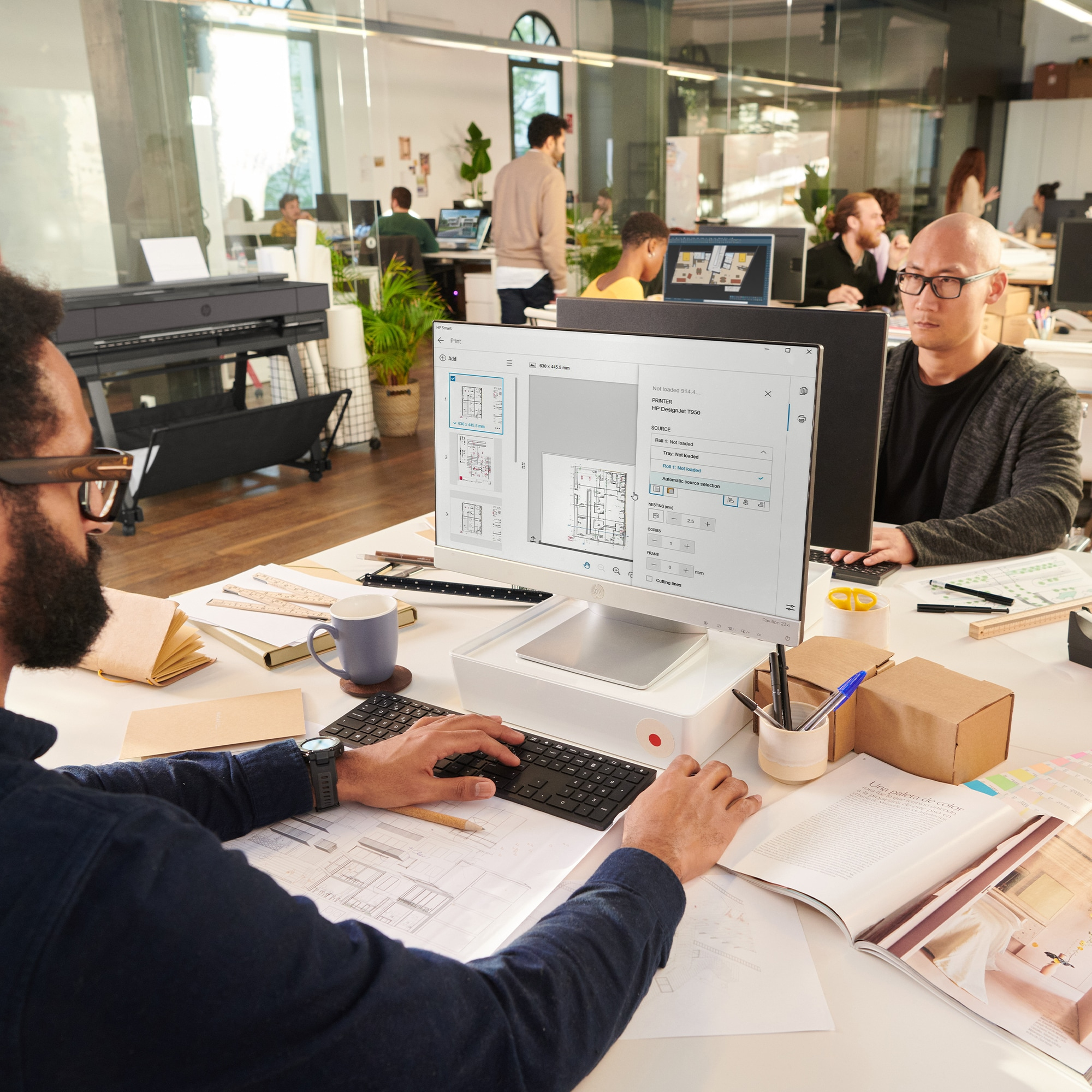 Des personnes travaillent sur des ordinateurs dans un bureau avec une imprimante grand format en arrière-plan.