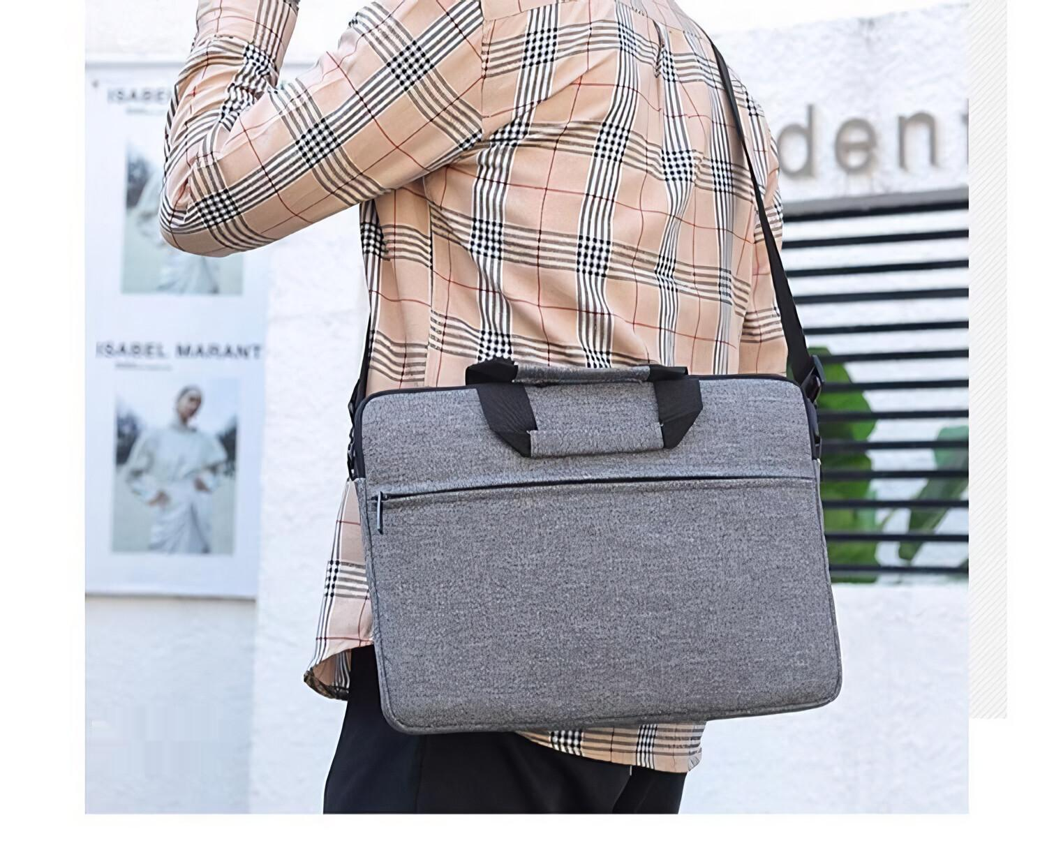 Eine Person mit einem karierten Hemd trägt eine graue Laptoptasche mit einem Schultergurt im Freien.