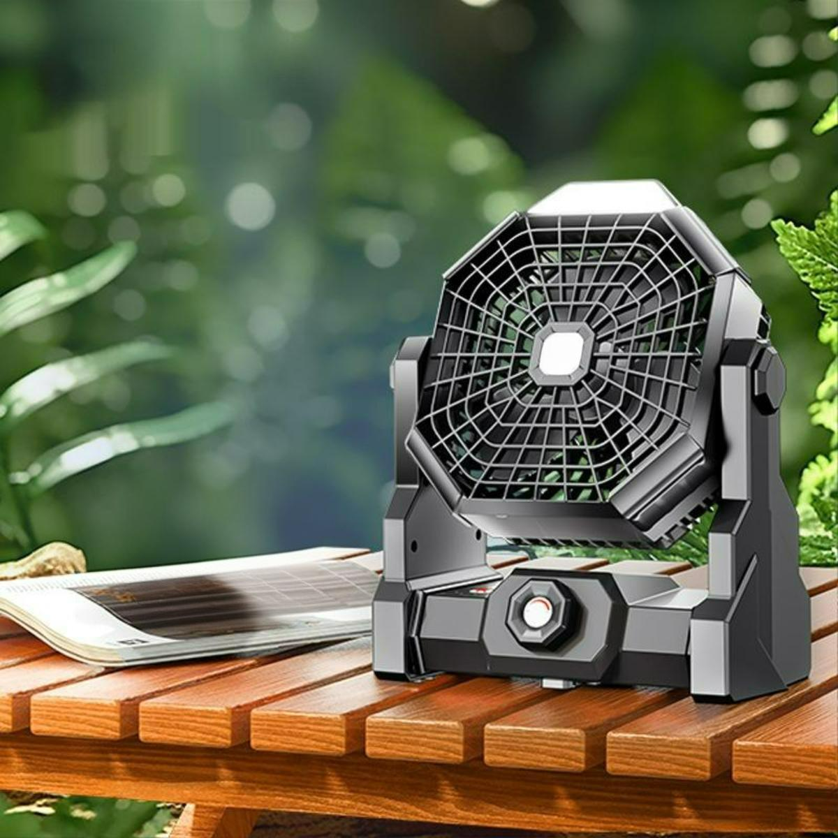 Ein schwarzer tragbarer Ventilator mit Licht oben steht draußen auf einem Holztisch.