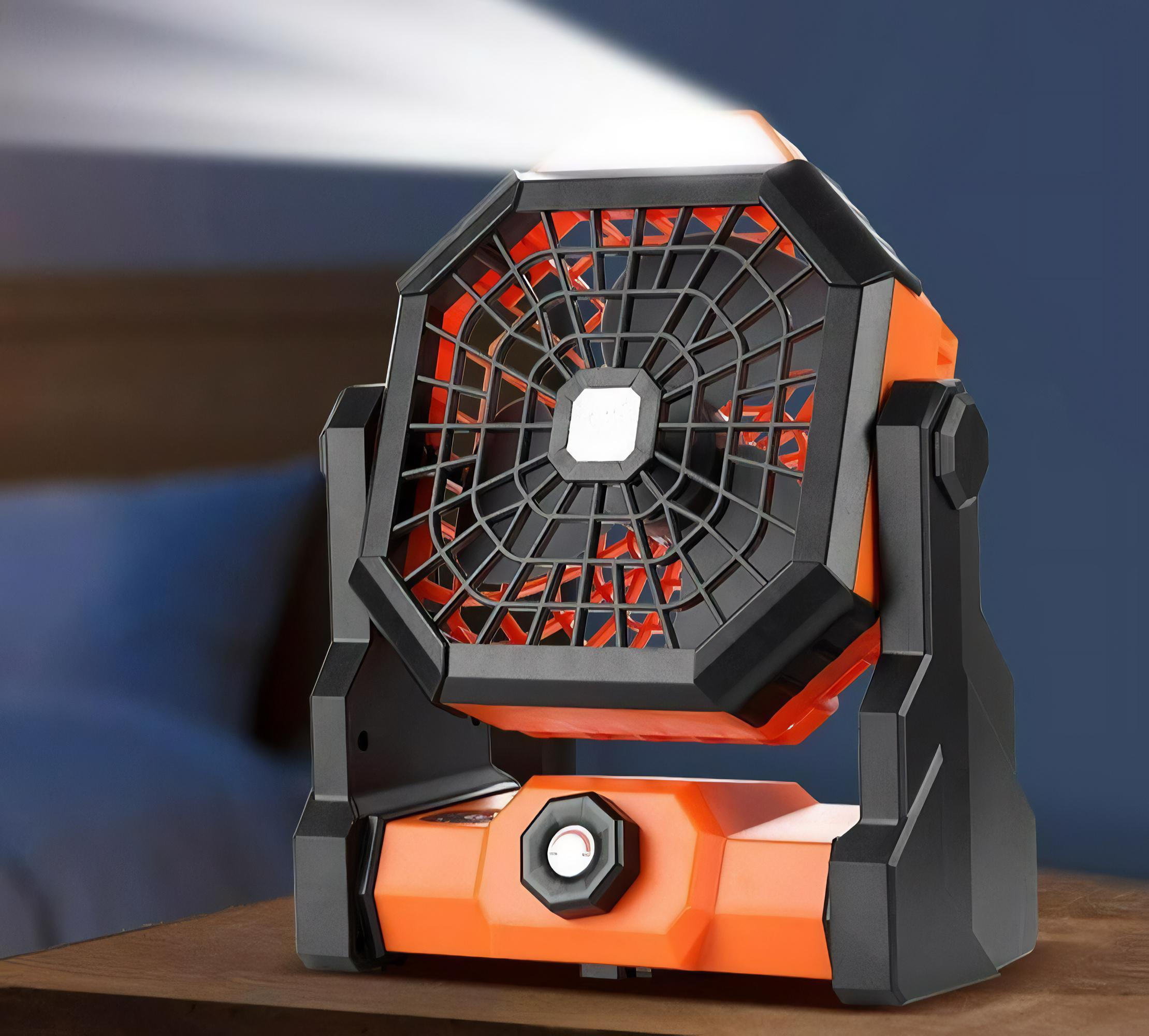 Ein orangefarbener tragbarer Ventilator mit Licht oben steht drinnen auf einem Holztisch.