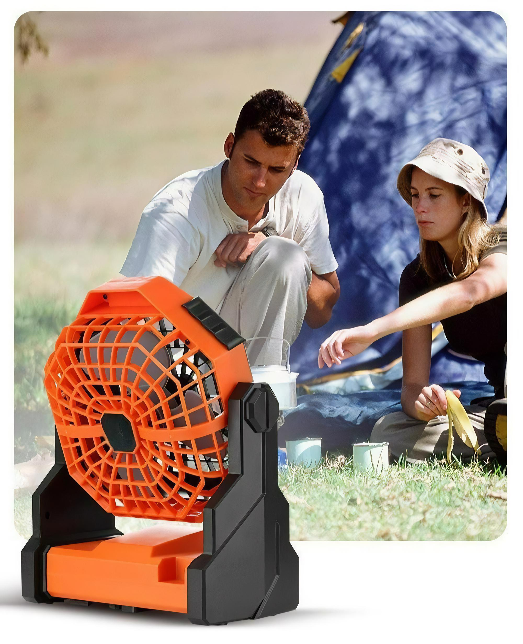 Ein orangefarbener und schwarzer Ventilator steht auf Gras. Menschen sind im Hintergrund, in der Nähe eines Zeltes.