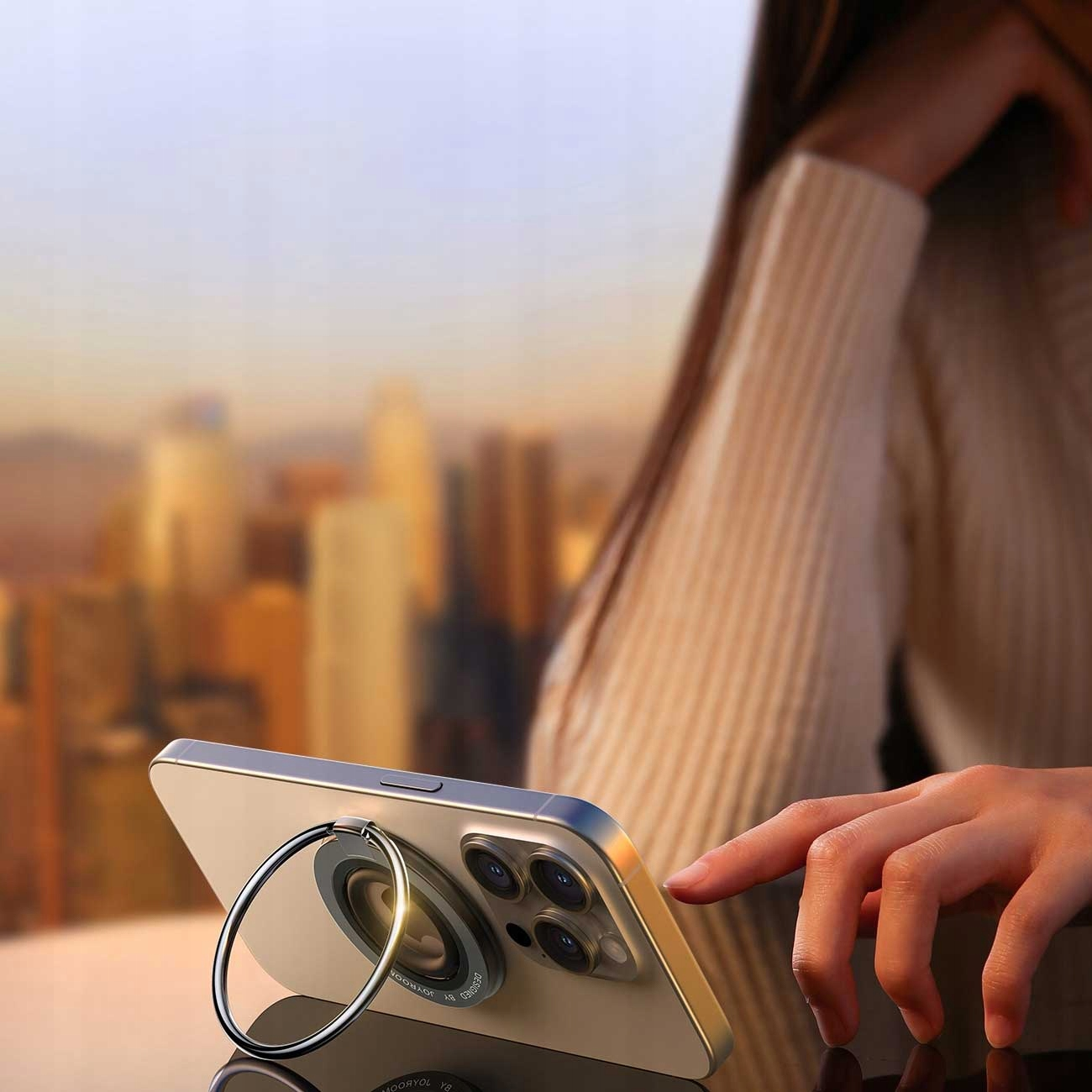 Ręka trzymająca telefon na stojaku z panoramą miasta w tle.
