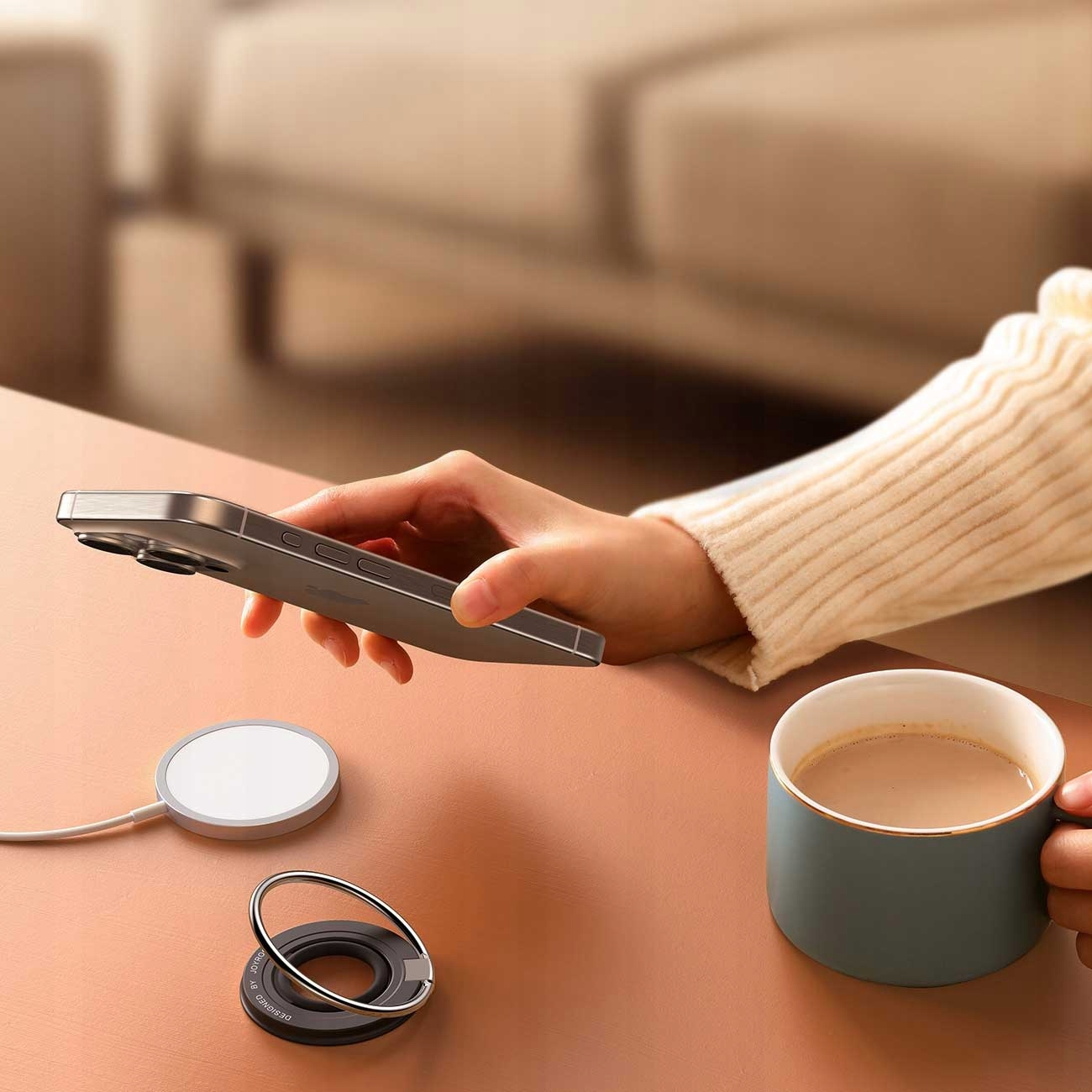 Osoba trzymająca telefon z podkładką ładującą, stojakiem na pierścień i kubkiem kawy.
