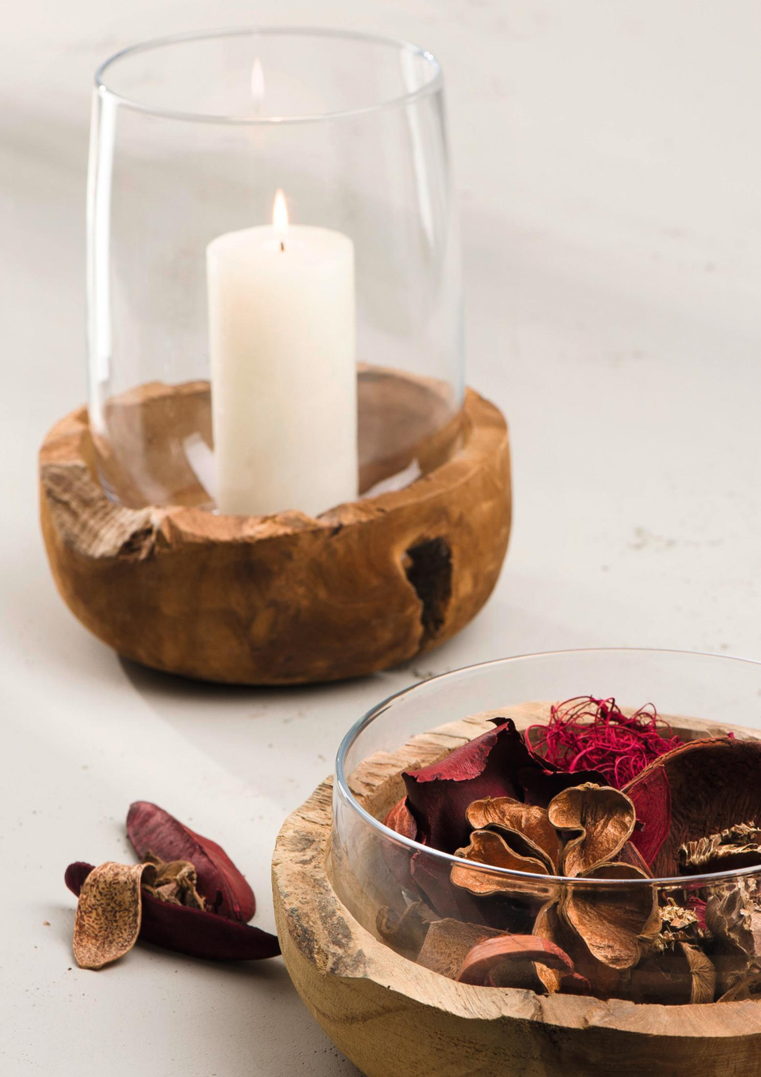 Eine brennende Kerze in einem Glas- und Holzhalter und eine Schale mit Potpourri auf einer weißen Oberfläche.