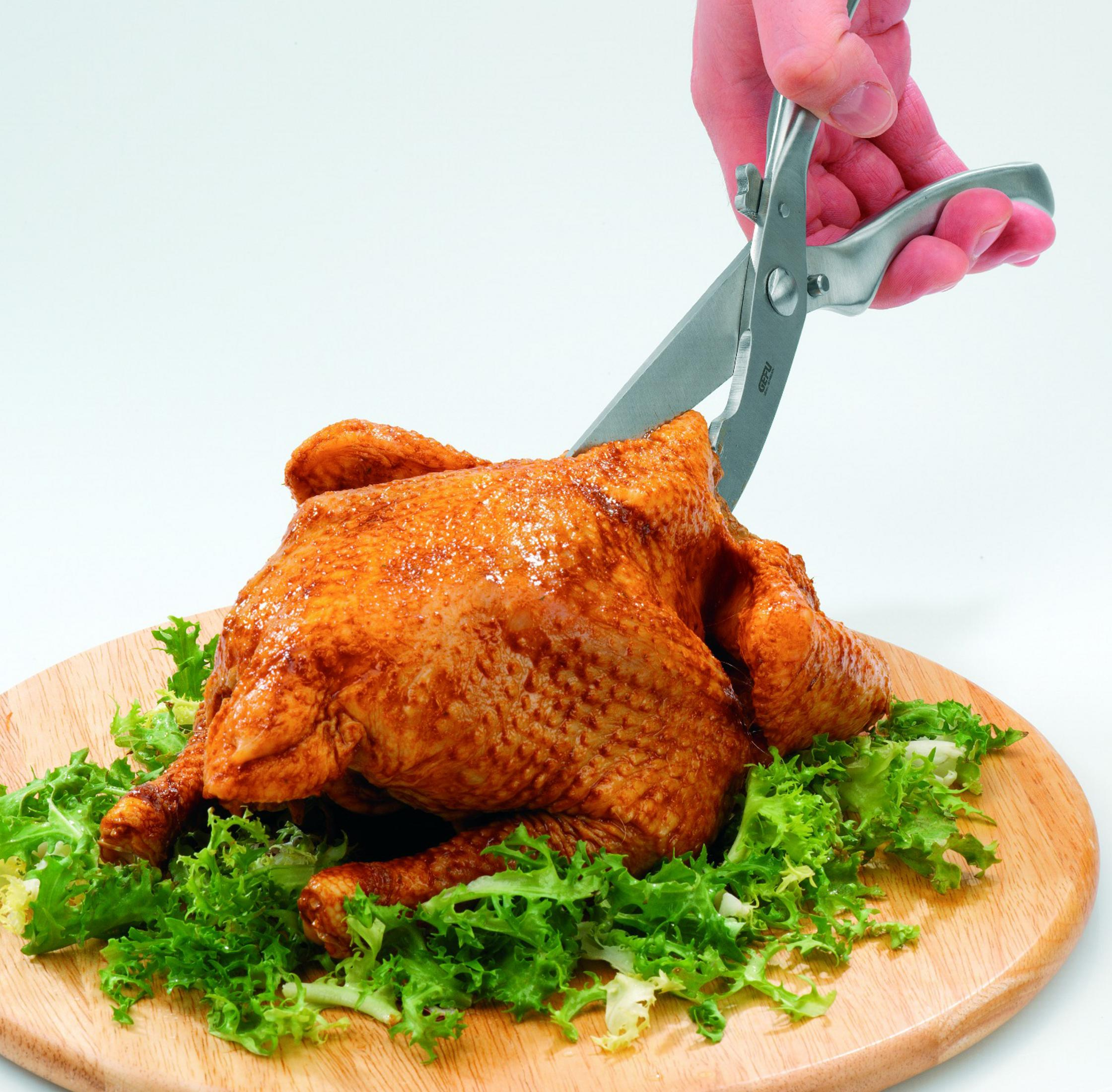 Forbici per pollame che tagliano un pollo arrosto su un tagliere di legno con lattuga.