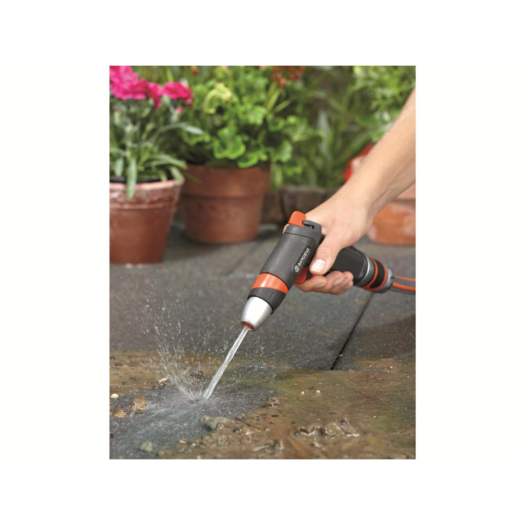 Hände halten eine GARDENA-Wasserpistole, die Wasser auf eine Steinoberfläche sprüht, mit Topfpflanzen.
