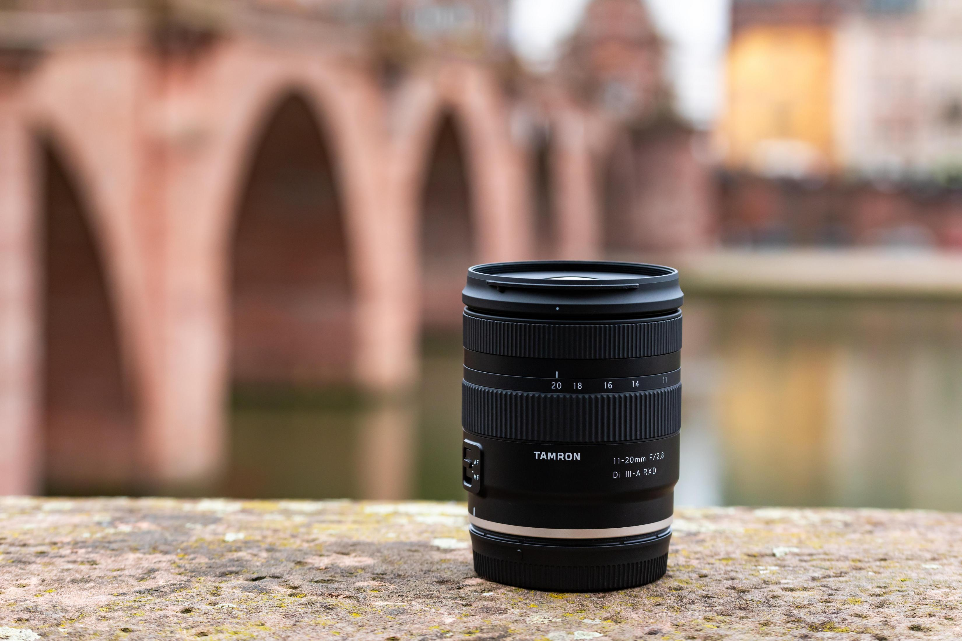 Tamron 11-20mm Kameraobjektiv auf Steinmauer, Brücke im Hintergrund unscharf.