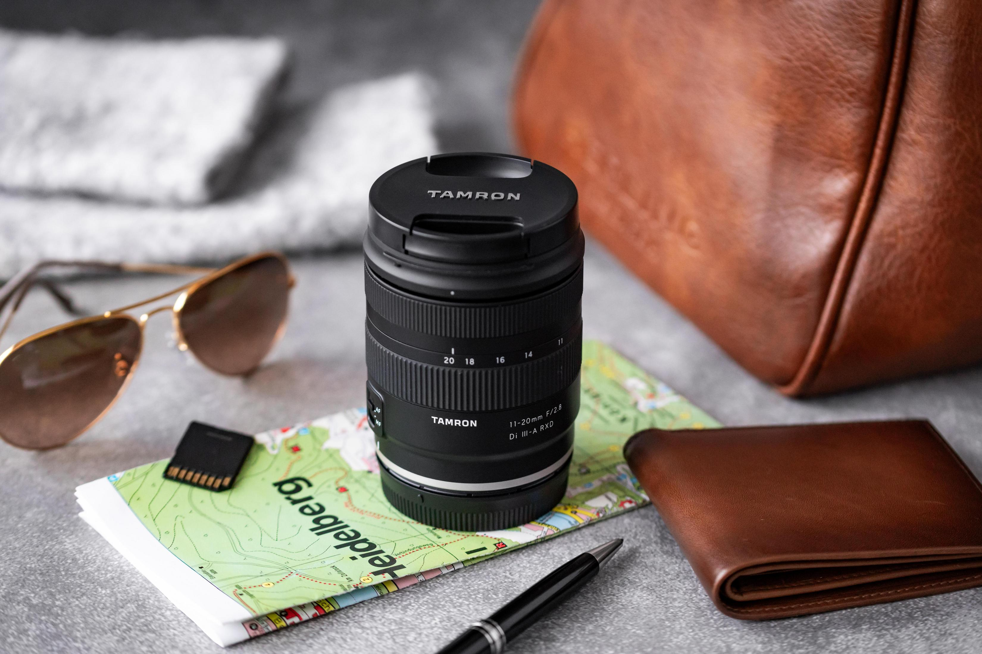 Tamron 11-20mm Objektiv mit Sonnenbrille, Karte, Geldbörse und Stift auf grauem Grund.
