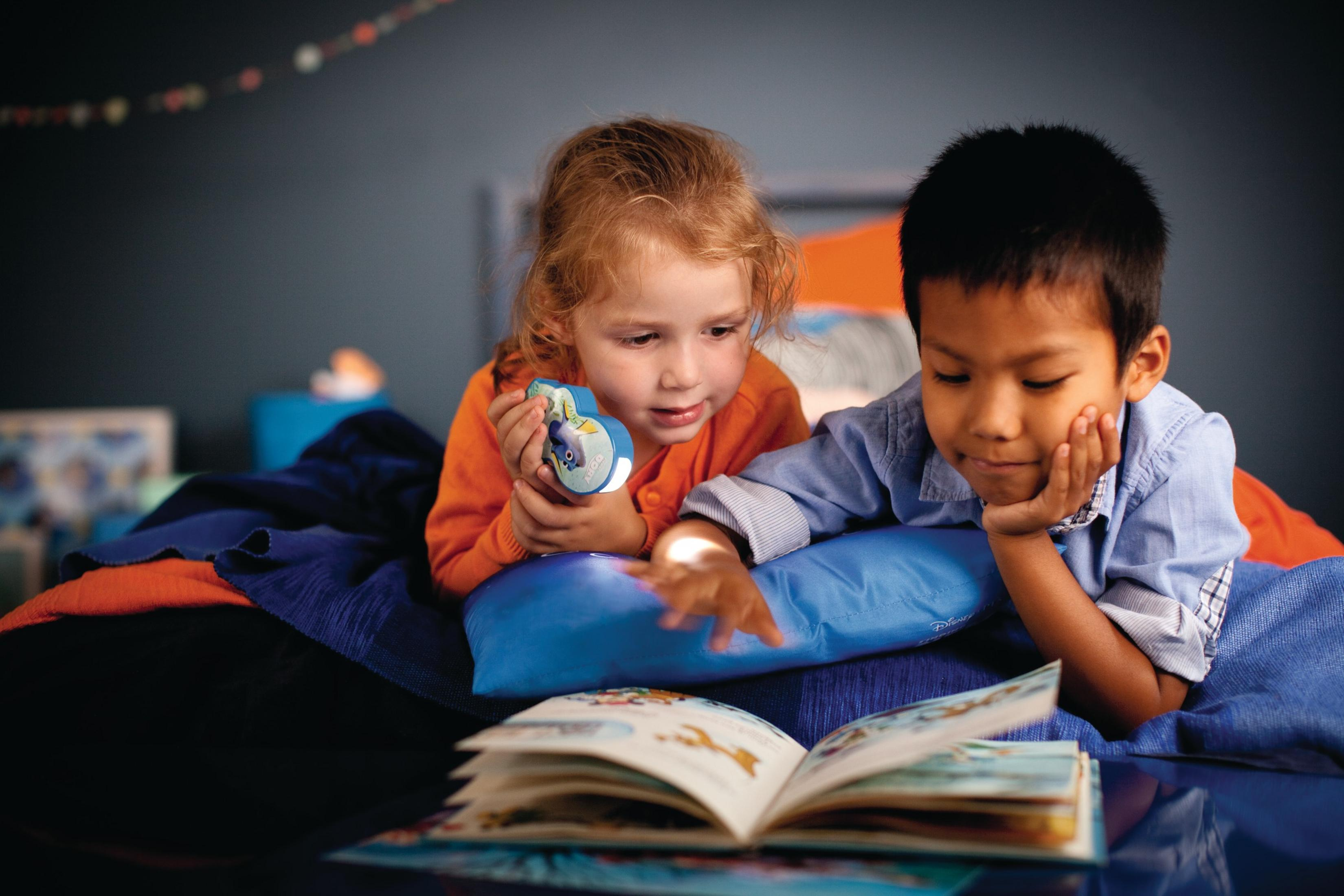 Zwei Kinder lesen ein Buch im Licht eines Nachtlichts im Dory-Design in einem schwach beleuchteten Raum.