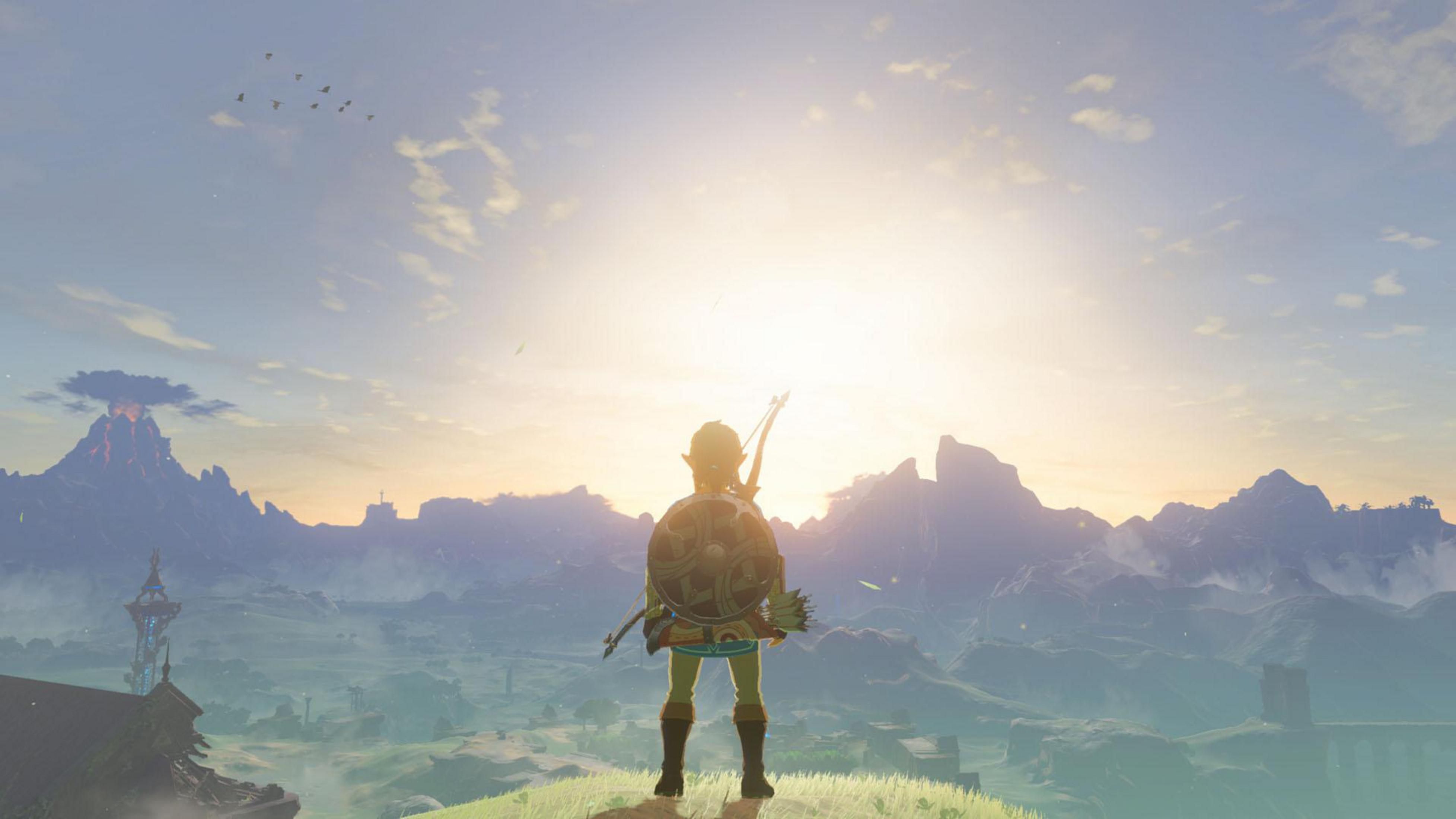 Link stoi na wzgórzu z widokiem na góry o wschodzie słońca w The Legend of Zelda: Breath of the Wild.