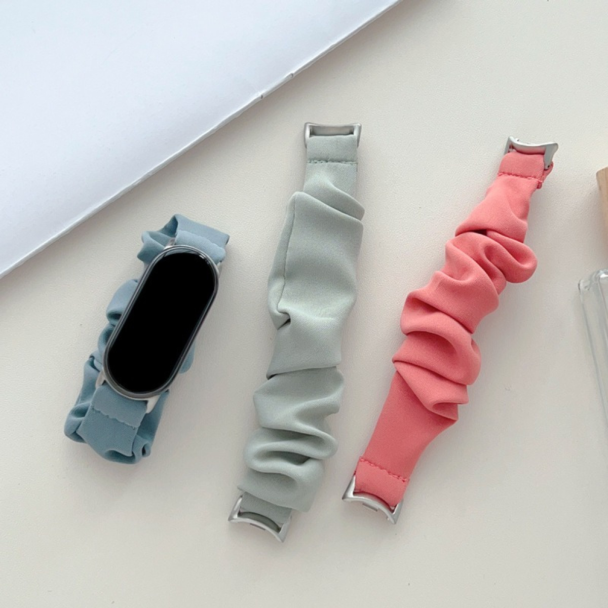 Tre cinturini per orologi stile scrunchie: blu chiaro, verde chiaro e rosa. Il cinturino blu tiene un orologio.