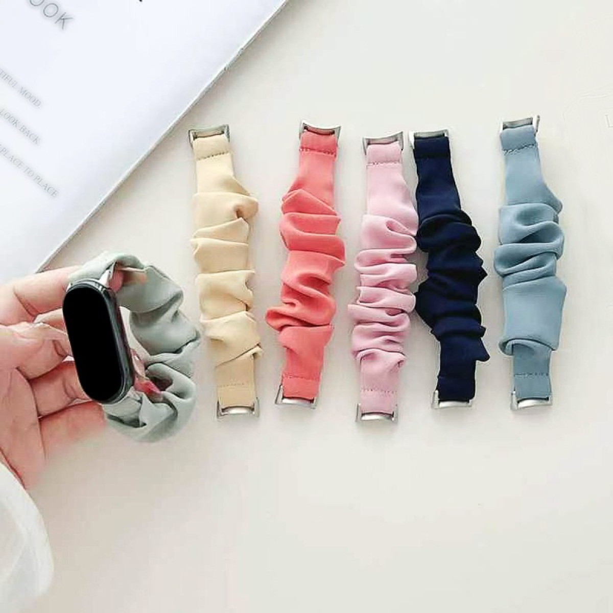 Cinturini per orologi in vari colori: verde chiaro, crema, rosa, blu navy e azzurro. Un orologio a sinistra.