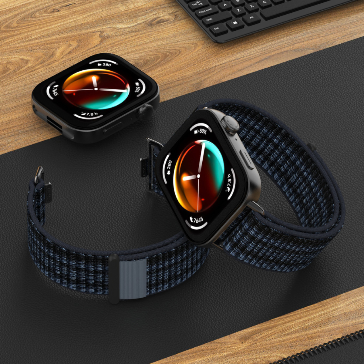 Due smartwatch con cinturini fantasia sono su una scrivania di legno accanto a una tastiera.