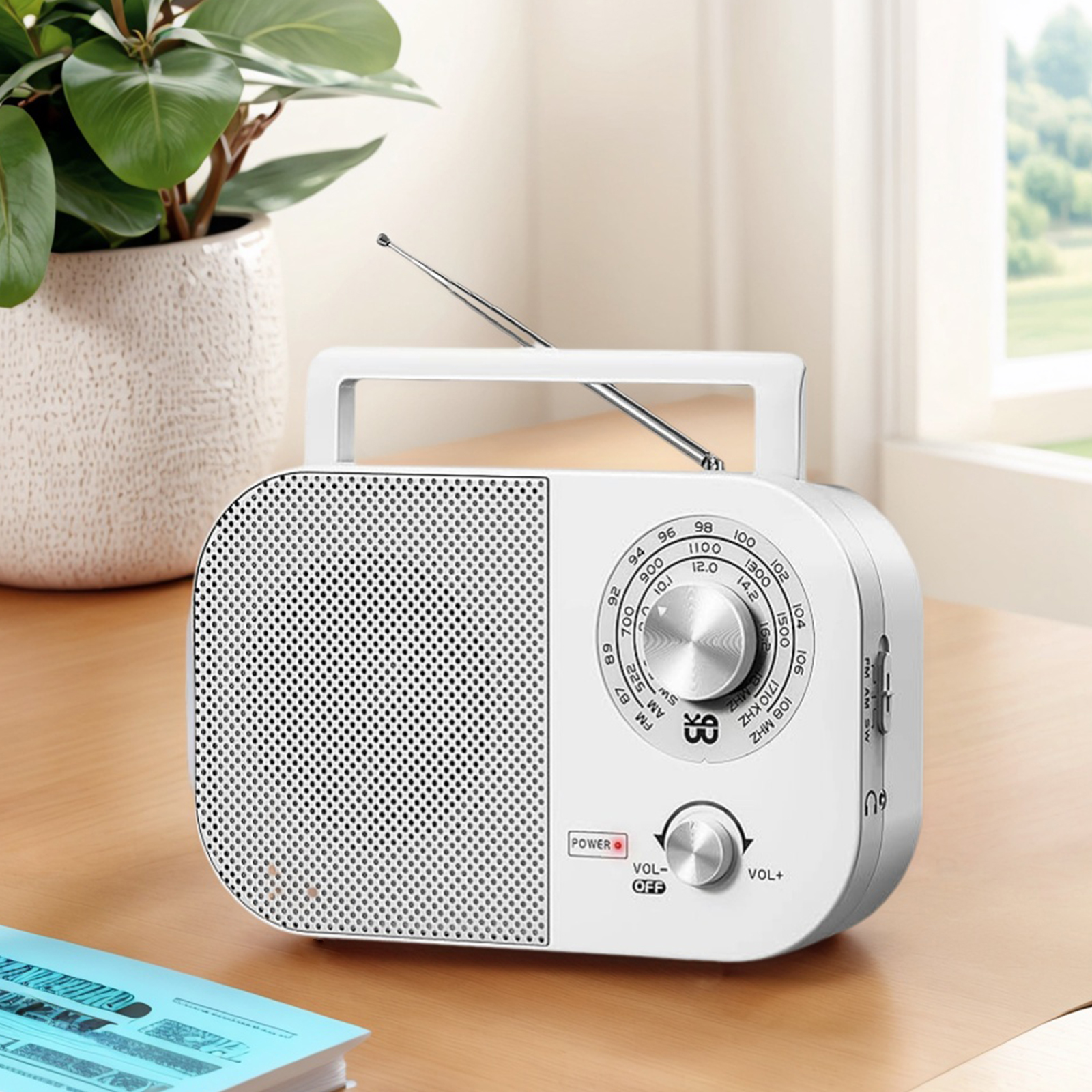Weißes tragbares Radio auf einem Holztisch in der Nähe einer Topfpflanze und eines Buches.
