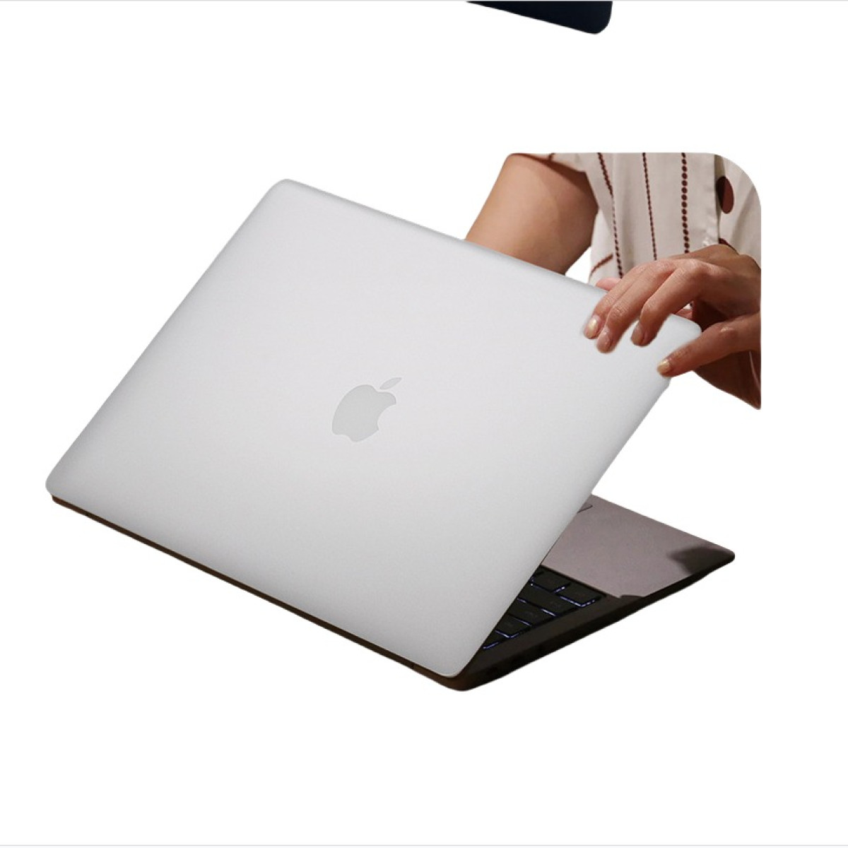 Ein silberner Laptop mit einem schwarzen Apple-Logo wird von einer Person auf einem weißen Hintergrund geöffnet.