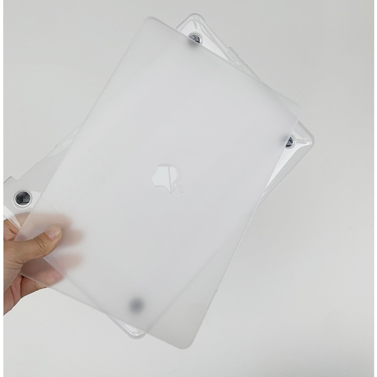 Eine Hand hält eine mattierte Laptop-Hülle mit Apple-Logo, wobei Eckdetails auf weißem Hintergrund zu sehen sind.