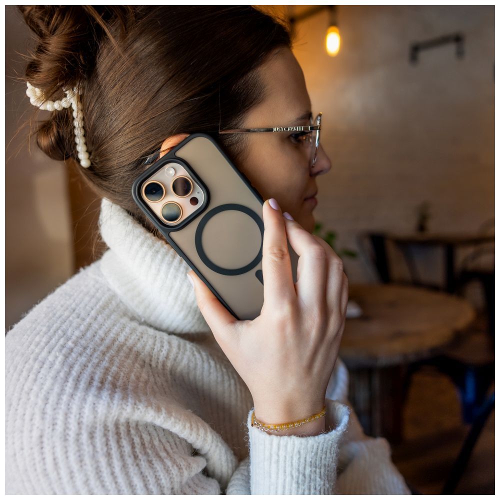 Frau telefoniert und hält ein Telefon mit Hülle. Sie trägt einen weißen Pullover und eine Brille, in einem Café.