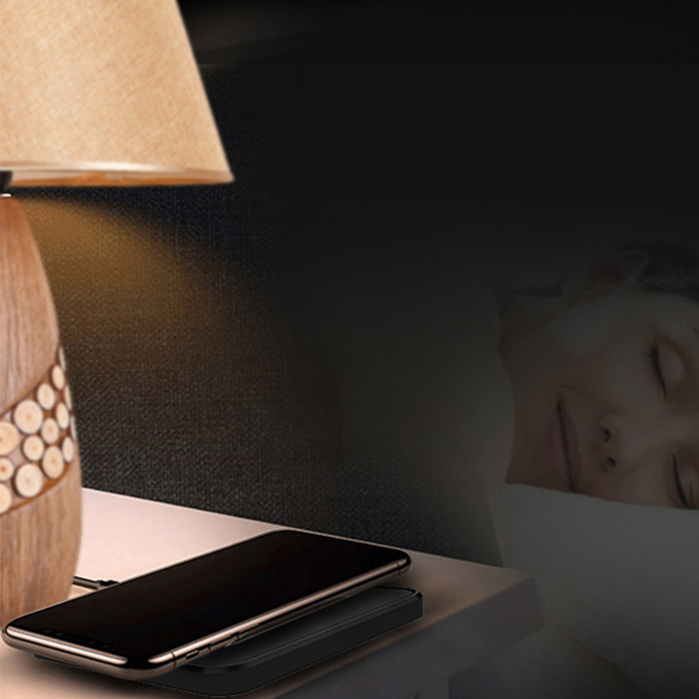 Ein Telefon, das auf einem kabellosen Ladepad neben einer Lampe auf einem Nachttisch auflädt.