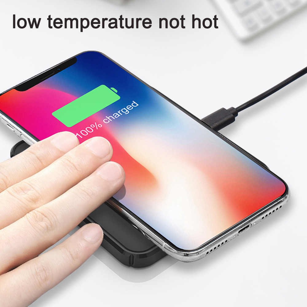 Eine Hand berührt ein Telefon, das auf einem kabellosen Ladepad auflädt und 100 % geladen anzeigt.