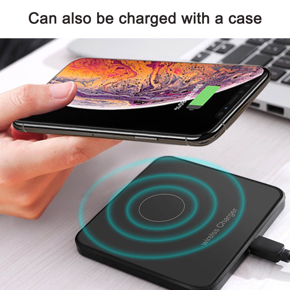 Eine Hand hält ein aufladendes Telefon über einem kabellosen Ladegerät auf einem Schreibtisch mit einem Laptop im Hintergrund.