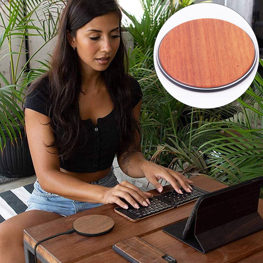 Eine Frau tippt auf einer Tastatur neben einem kabellosen Ladepad auf einem Holztisch, umgeben von Pflanzen.