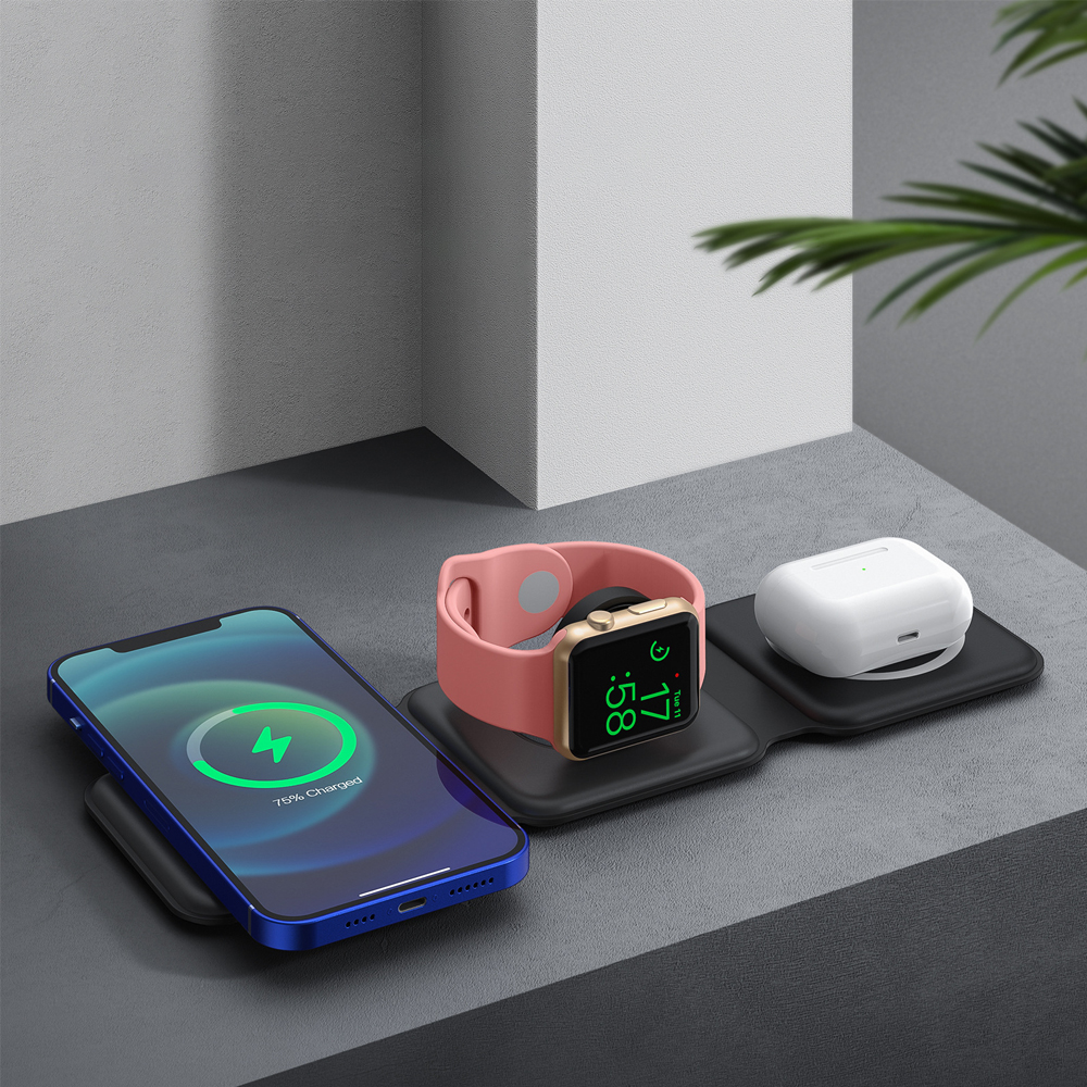 Ein schwarzes, zusammenklappbares Drei-in-Eins-Wireless-Ladegerät, das ein Telefon, eine Uhr und Ohrhörer auf einer grauen Oberfläche auflädt.