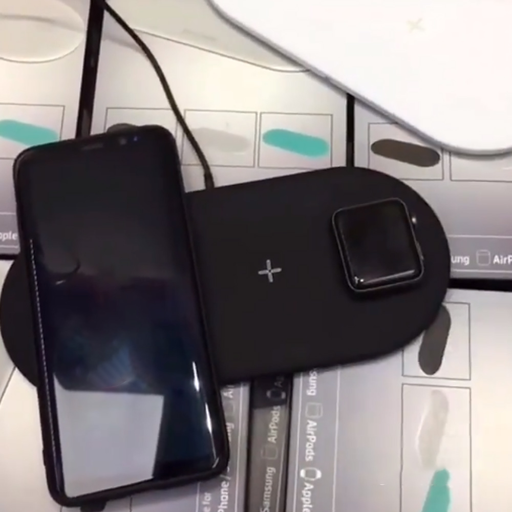 Ein Telefon und eine Uhr, die auf einem schwarzen kabellosen Ladepad auf Kartons geladen werden.