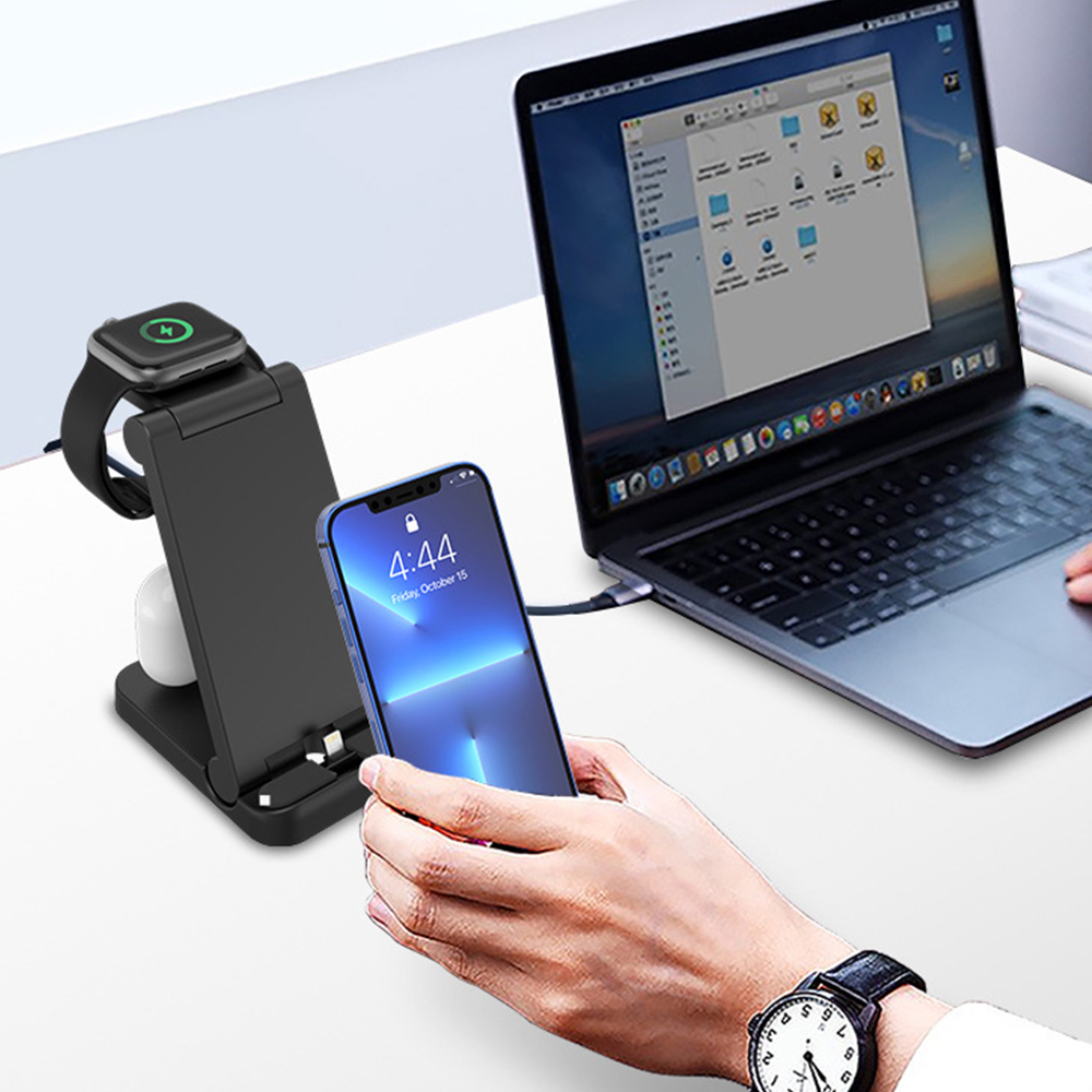 Eine Ladestation auf einem Schreibtisch lädt ein Telefon, eine Uhr und Ohrhörer neben einem Laptop auf.