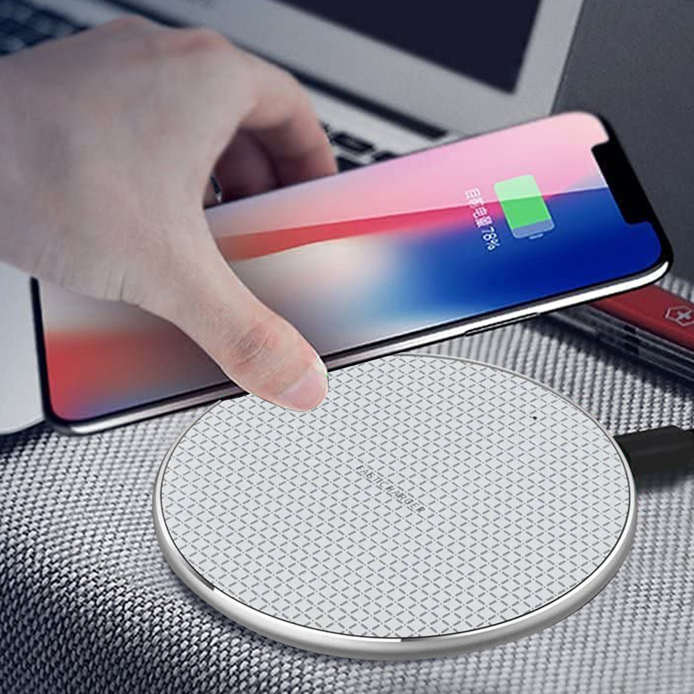 Eine Hand legt ein Telefon auf ein weißes kabelloses Ladegerät auf einer grauen Oberfläche neben einem Laptop und einem Stift.