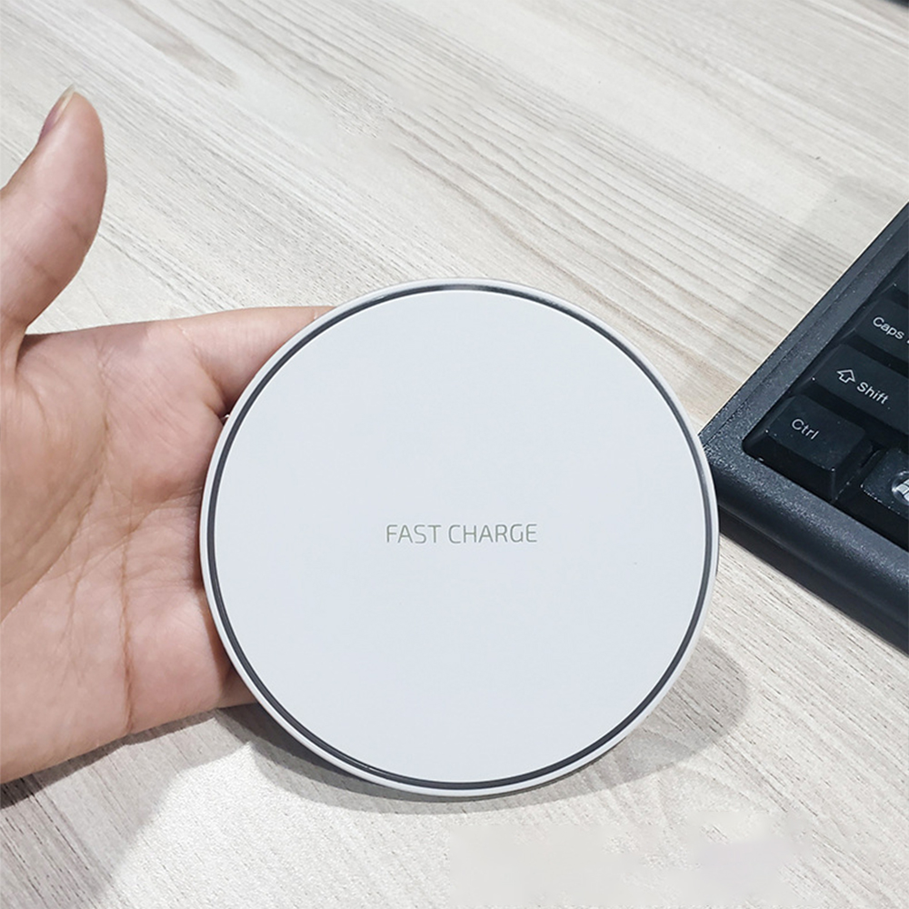 Eine Hand hält ein weißes kabelloses Ladepad mit dem Text „Fast Charge“ neben einer Tastatur.