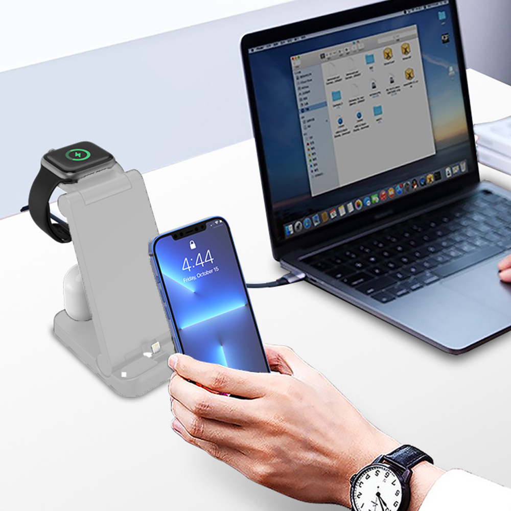Ein Schreibtisch-Setup mit einem Laptop, einem Telefon und einer Ladestation, einschließlich einer Smartwatch und kabellosen Ohrhörern.