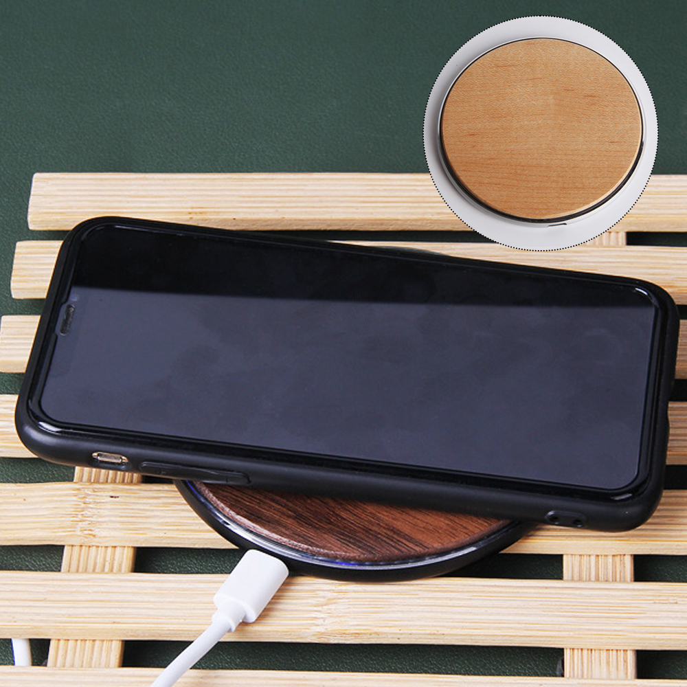 Ein schwarzes Smartphone wird auf einem kabellosen Ladegerät aus Holz mit einem weißen USB-Kabel aufgeladen.