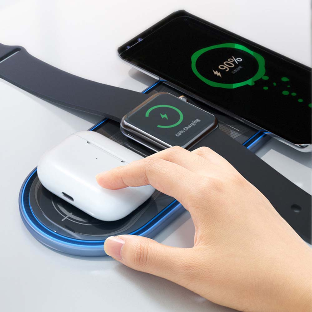 Eine Hand legt Ohrhörer auf einen Ladeständer mit einer Uhr und einem Telefon, die alle den Ladestatus anzeigen.