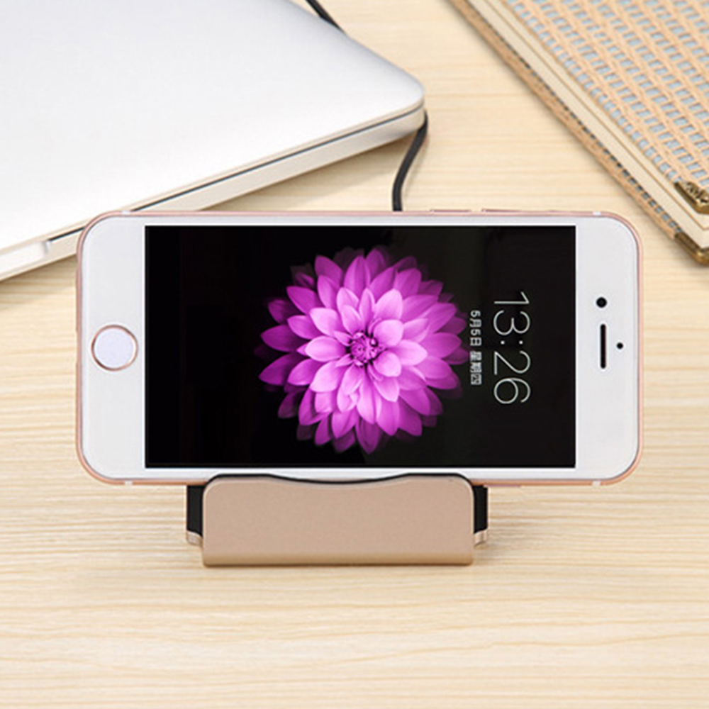 Ein Telefon mit einem Blumenhintergrundbild ist in einer goldfarbenen Ladestation auf einem Schreibtisch aus Holz angedockt.