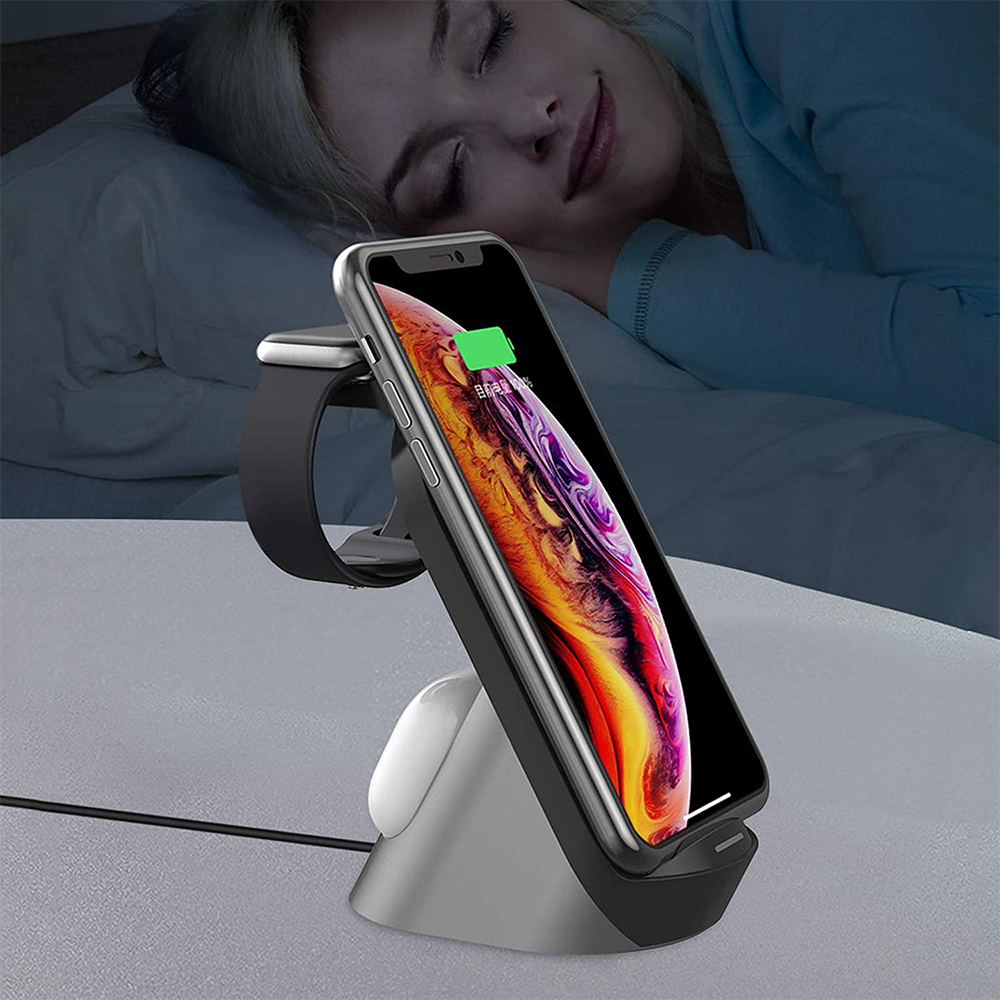 Ein Telefon und eine Uhr laden auf einem Ständer neben einer schlafenden Person in einem dunklen Raum.
