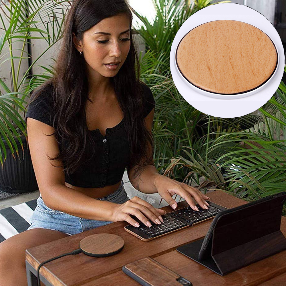 Frau benutzt Tastatur in der Nähe eines runden kabellosen Ladegeräts aus Holz in einem Raum mit Pflanzen.
