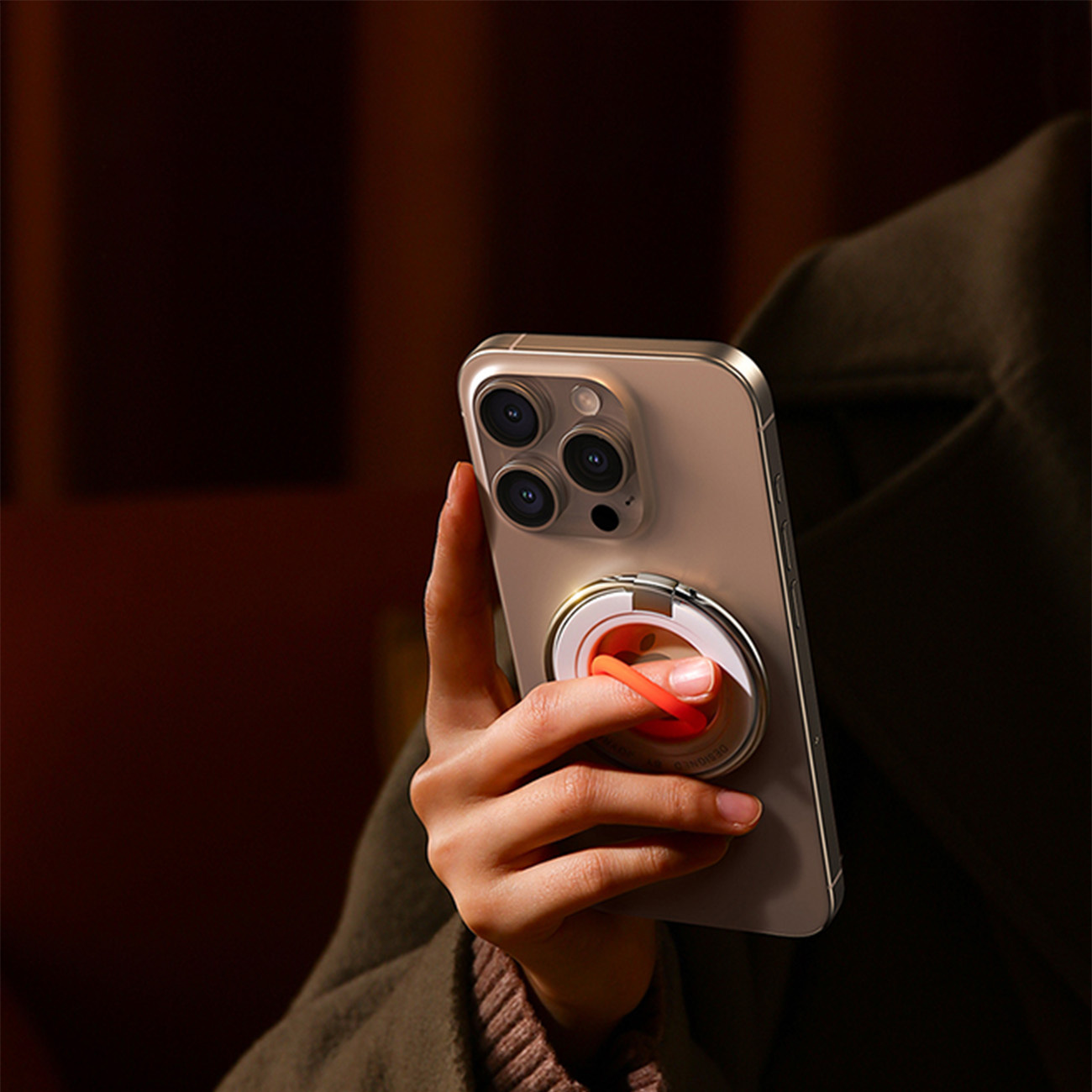 Dłoń trzyma telefon z uchwytem na pierścień. Telefon ma złotą ramkę i wiele aparatów.