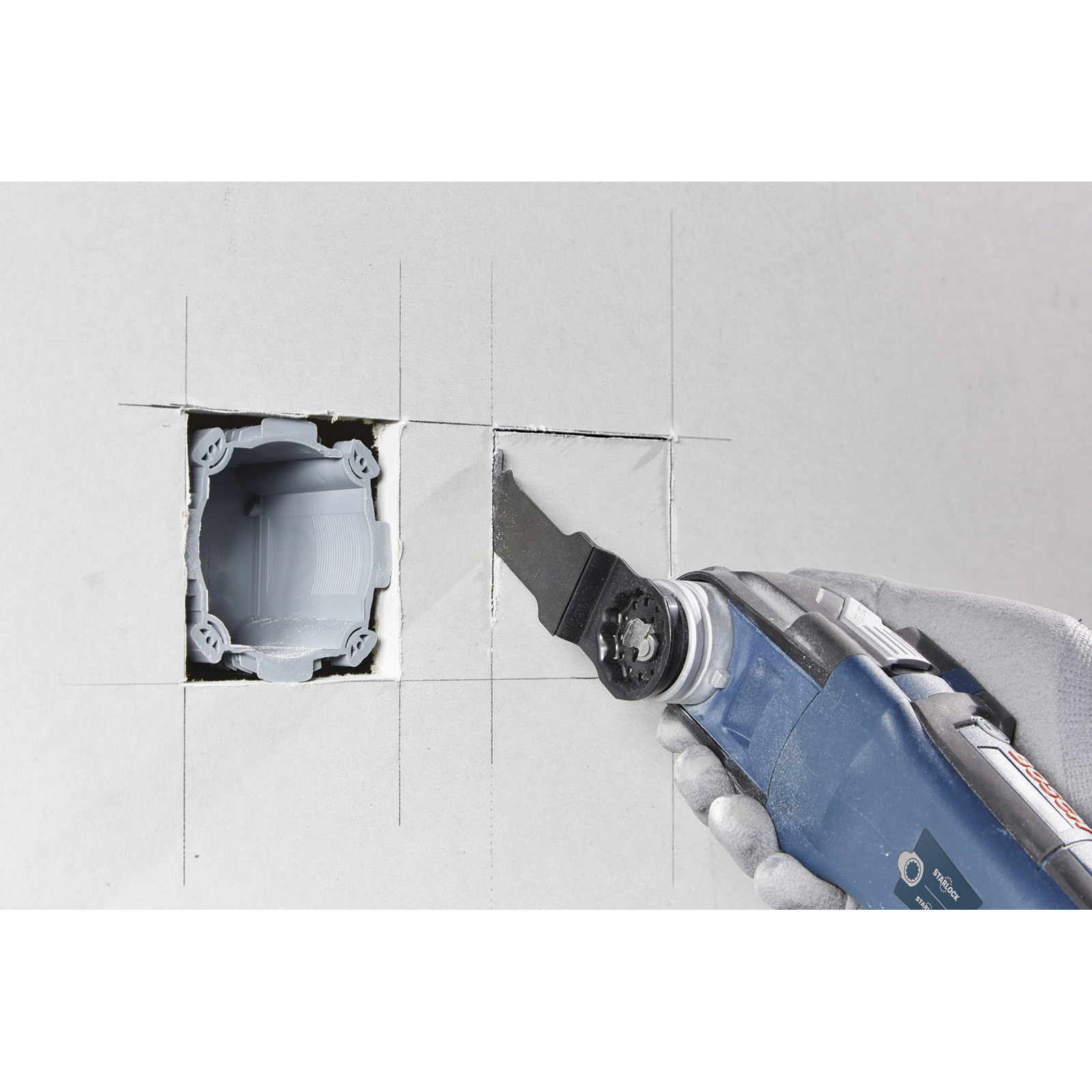 A blue oscillating multi-tool cutting into a wall next to a gray electrical box.