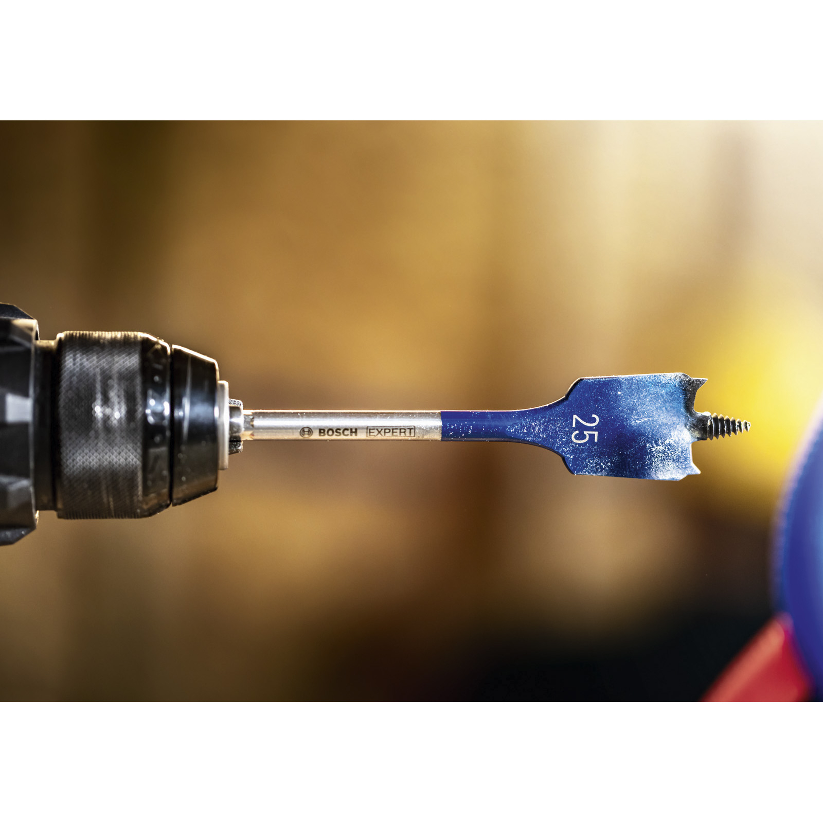 Niebieskie wiertło płaskie jest przymocowane do wiertarki. Wiertło ma oznaczenie 25, widoczna jest nazwa marki.