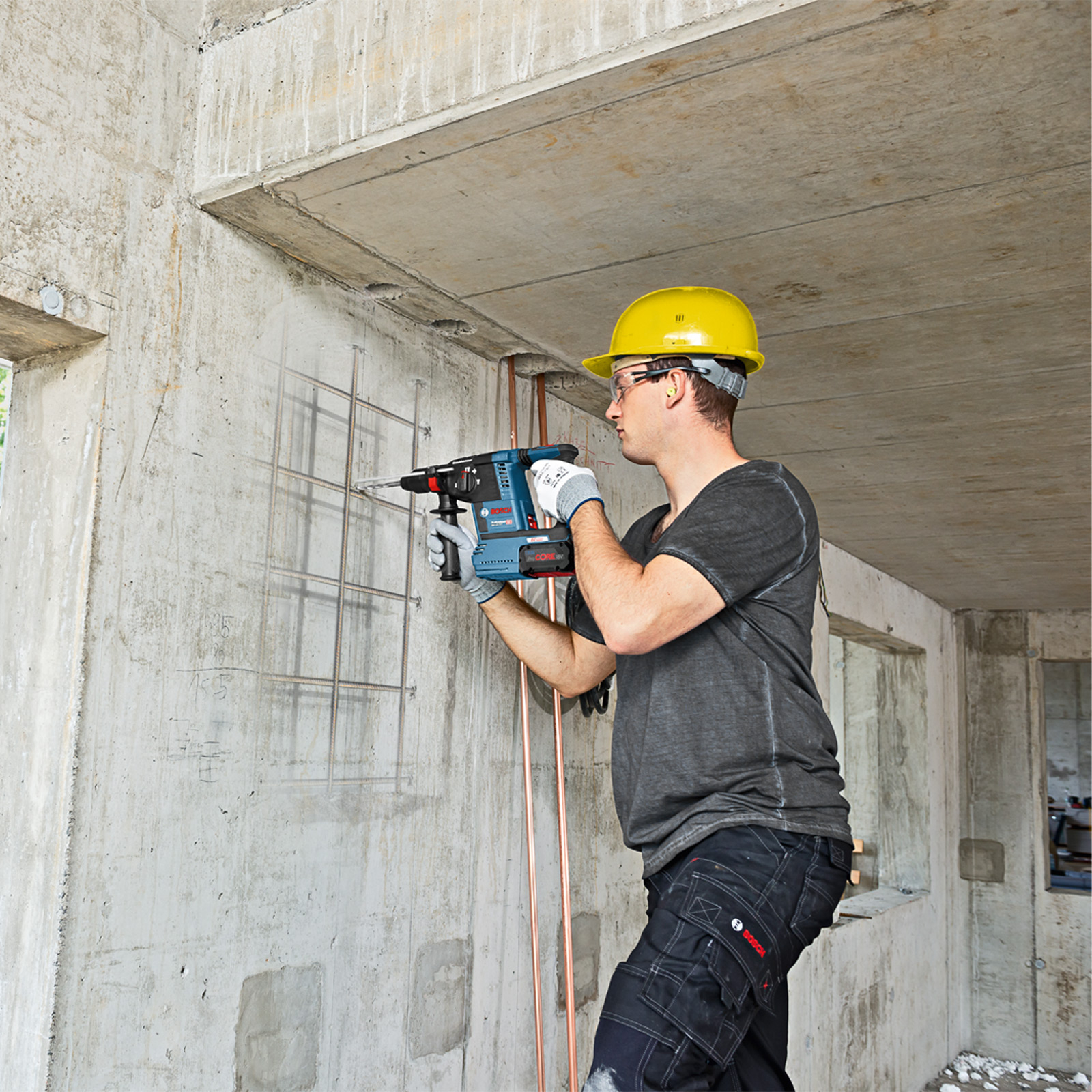 Ein Mann benutzt einen Bohrhammer. Er steht auf einer Betonkonstruktion und bohrt hinein.