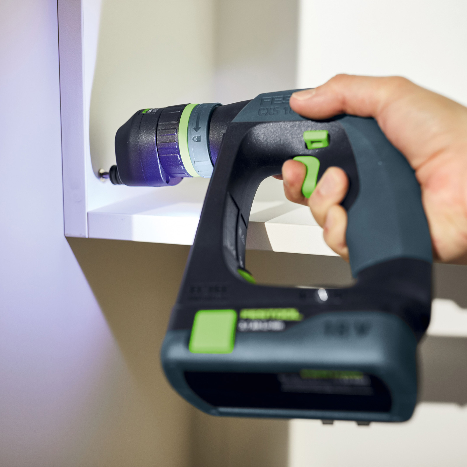 Osoba używa wiertarki do wkręcania śruby w białą szafkę. Wiertarka jest czarna i zielona.