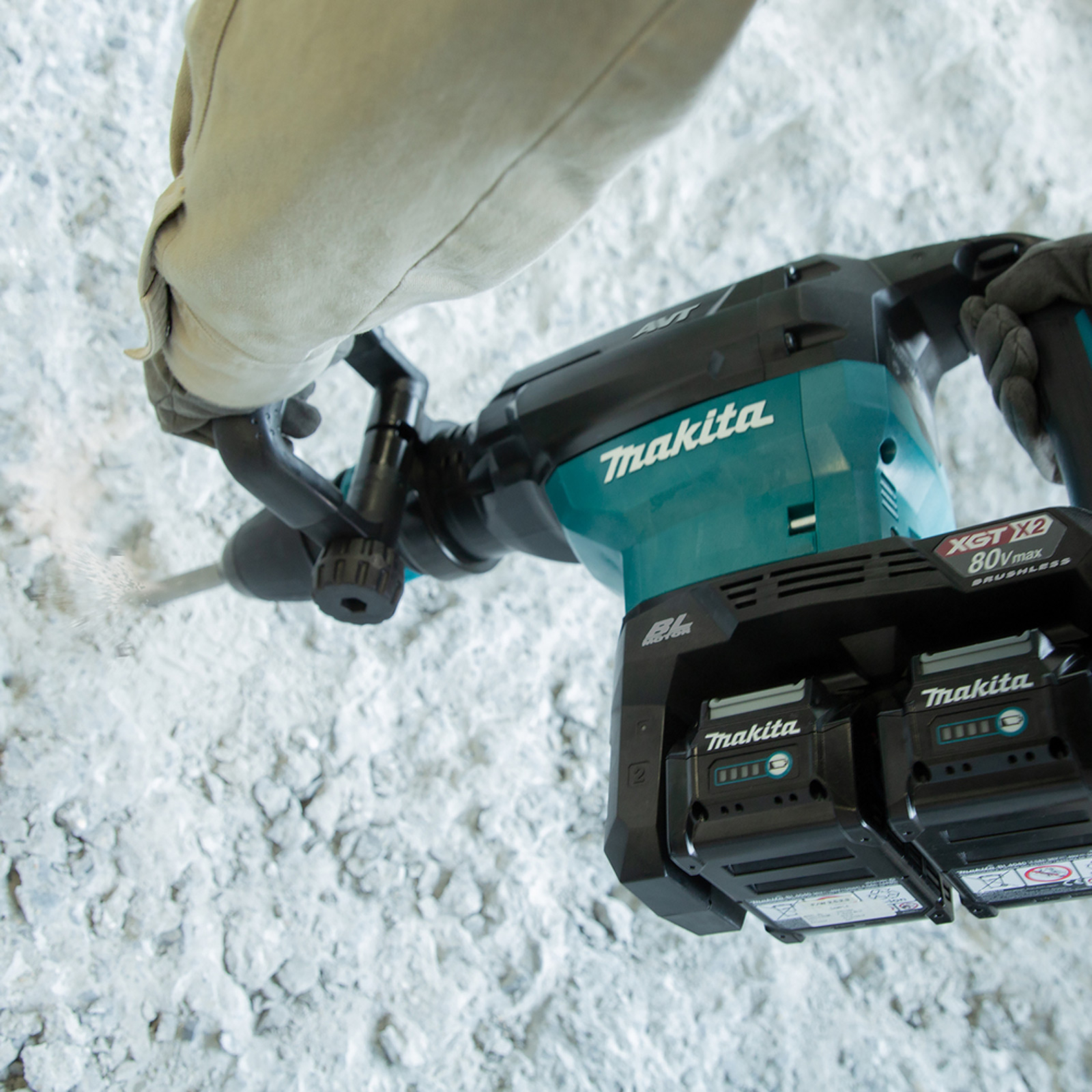 Una persona usa un martello perforatore Makita su una superficie di pietra bianca. La polvere è visibile. Batterie Makita in posizione.