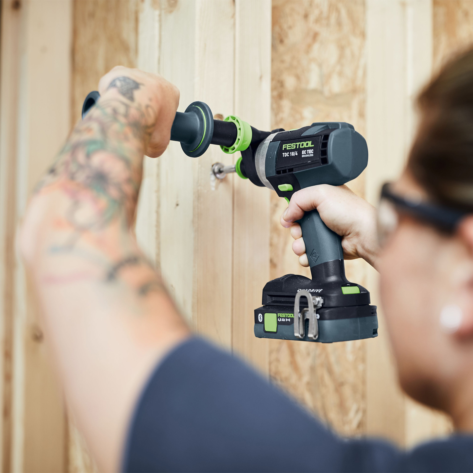 Un hombre usando un taladro Festool para instalar un tornillo en madera. El taladro es gris y verde.
