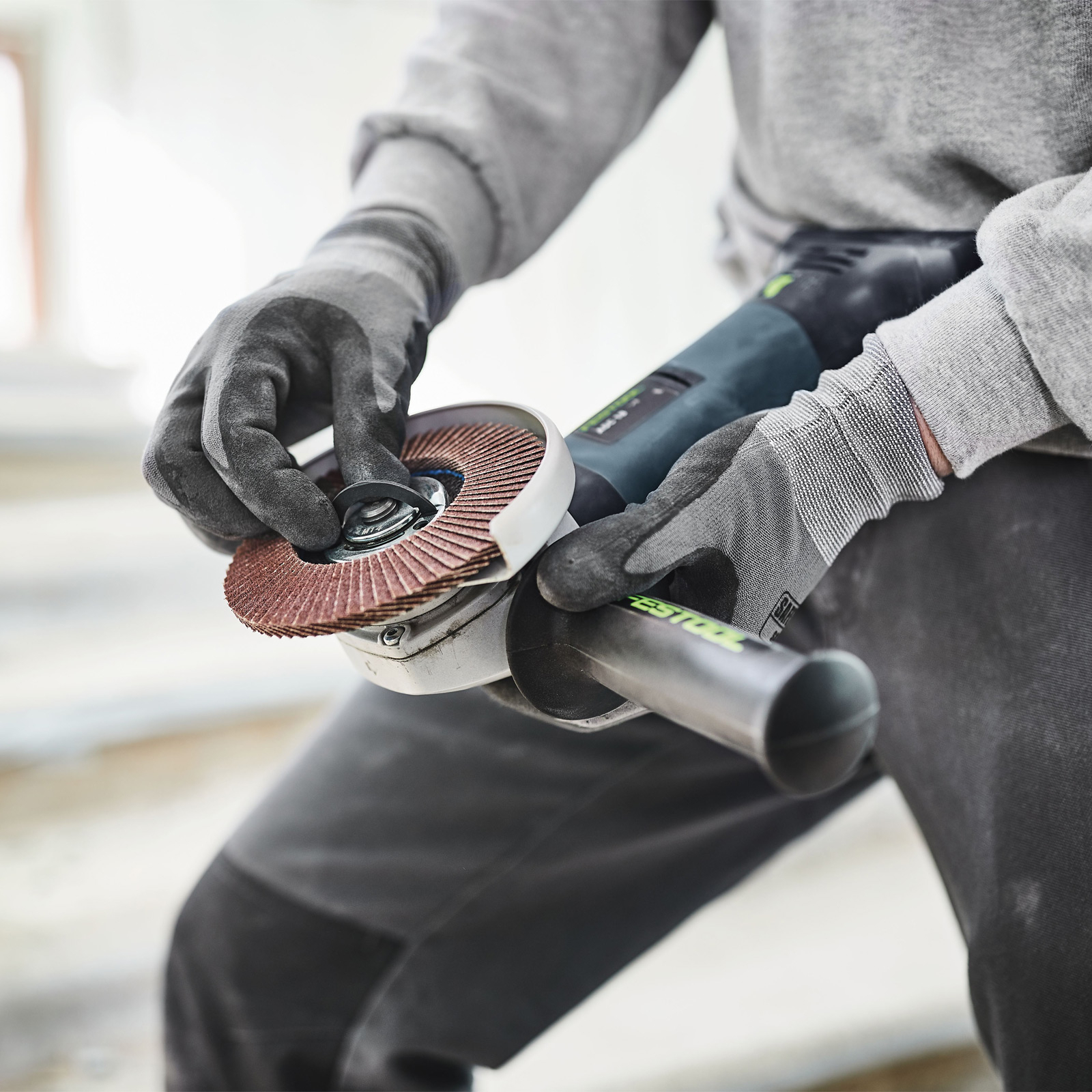 Una persona con guantes está usando una amoladora angular Festool para esmerilar una tubería de metal en un taller.