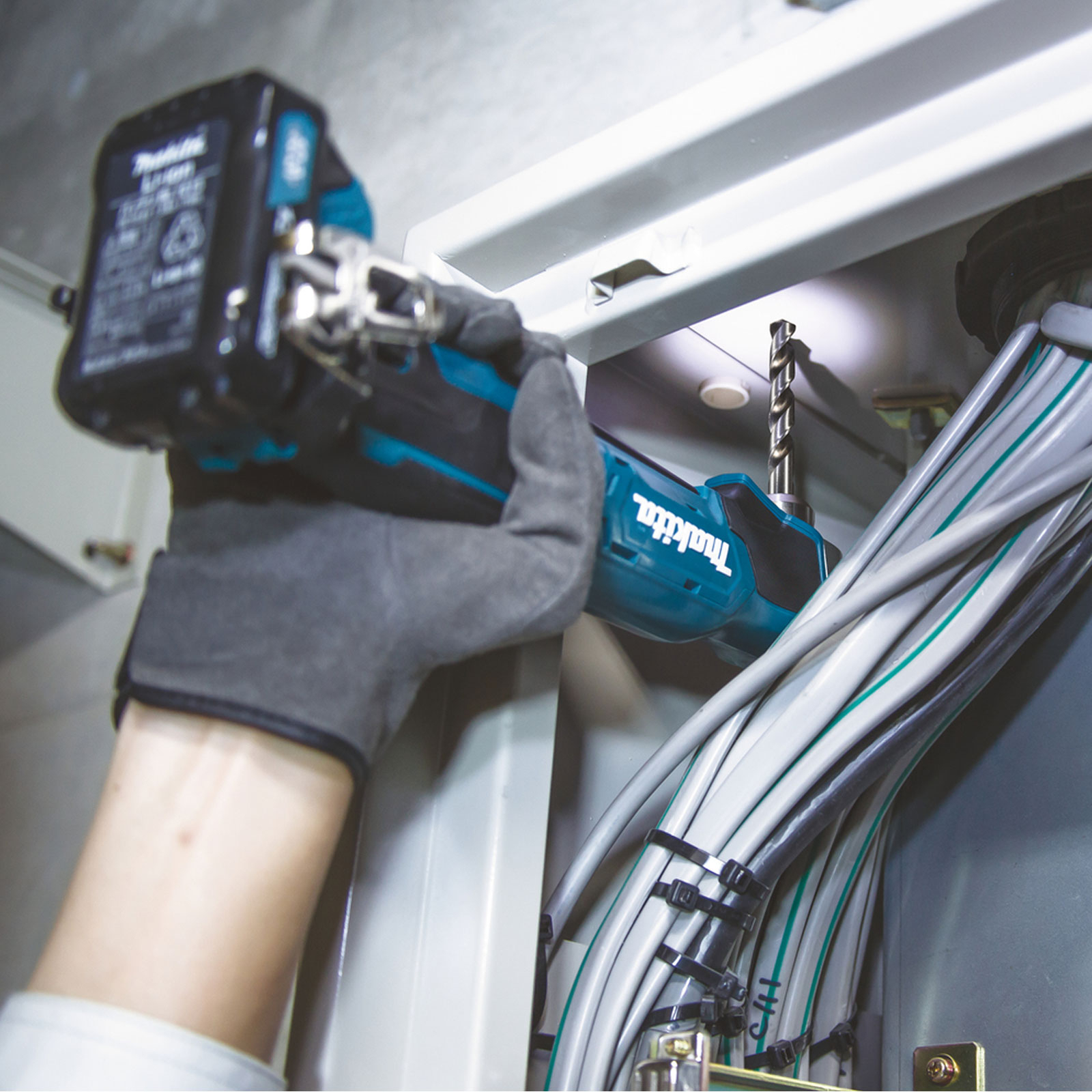 Una mano usando un taladro Makita para taladrar en un armario, con cables visibles.